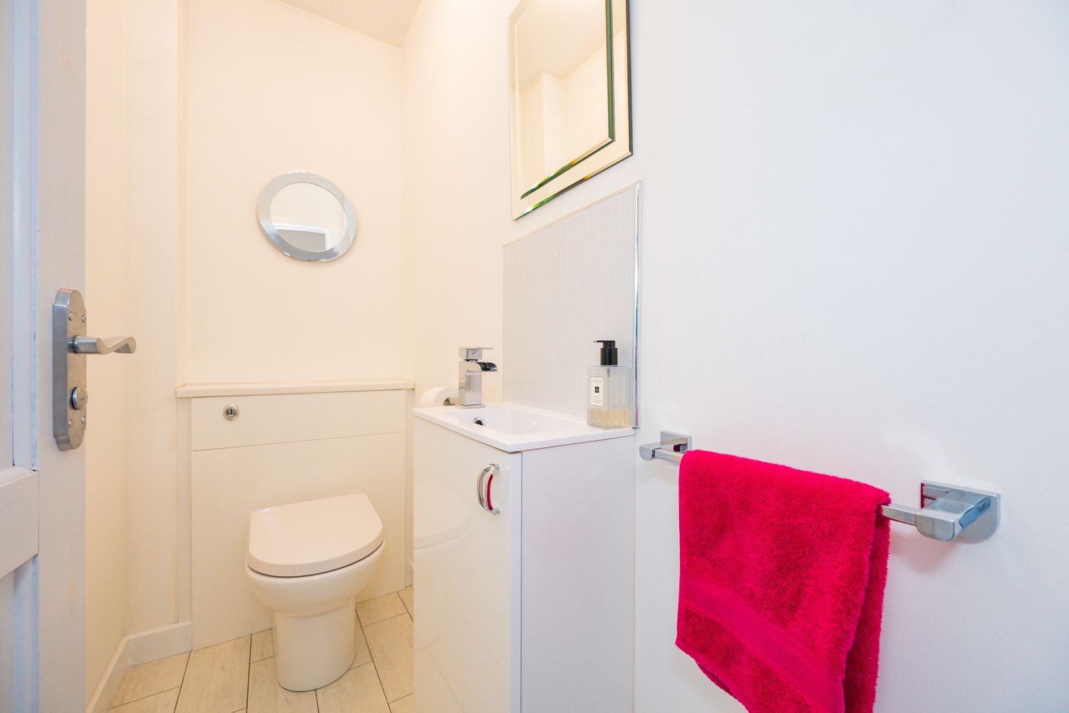 Small white bathroom with toilet, pedestal sink, and bright red towel hanging on chrome fixture.