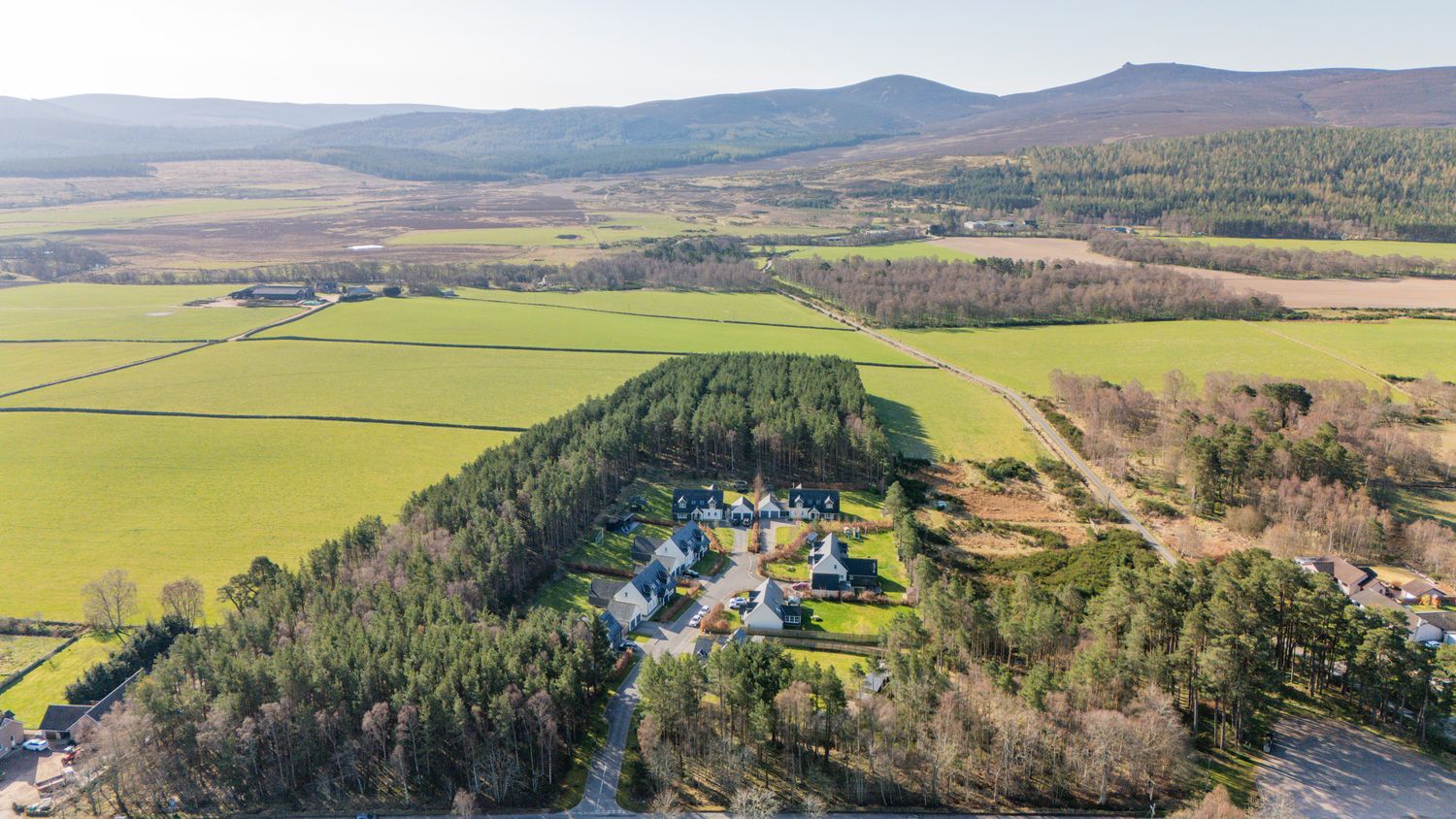 Aerial perspective of a countryside property with blue-roofed buildings amid rolling farmland and mountains.