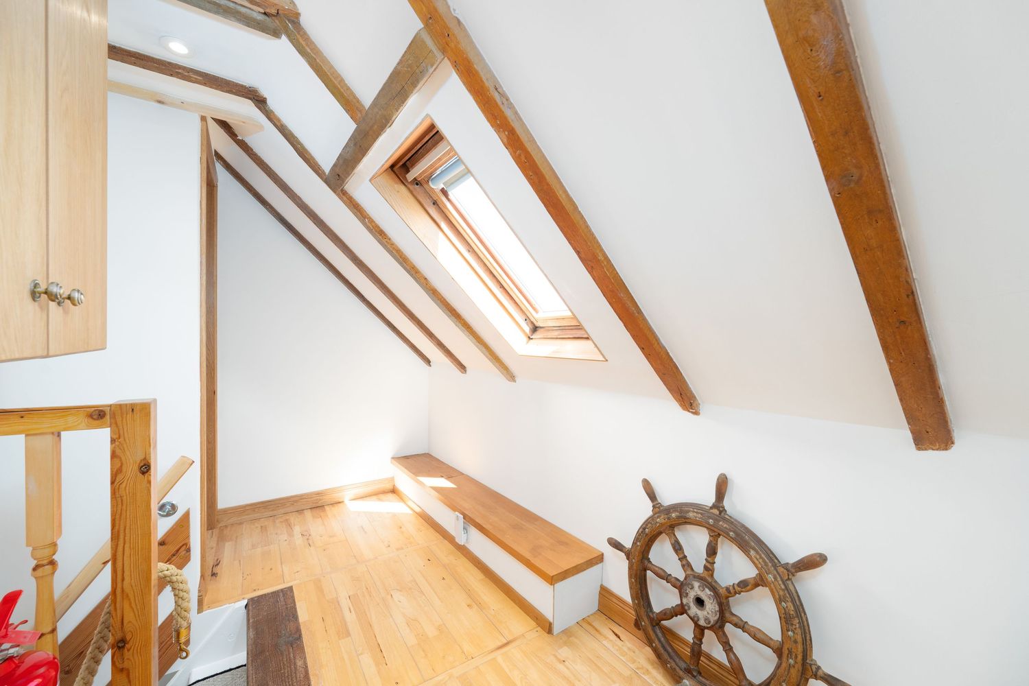 Attic room with exposed wooden beams, skylights and decorative ship's wheel on the wall.