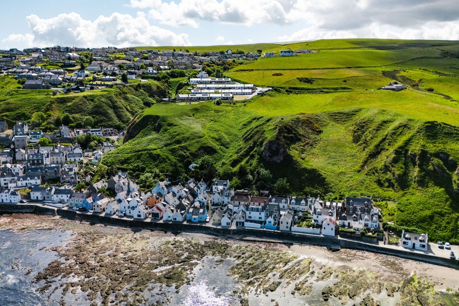 Aerial view of a coastal village nestled on green cliffs with white buildings along the shoreline.