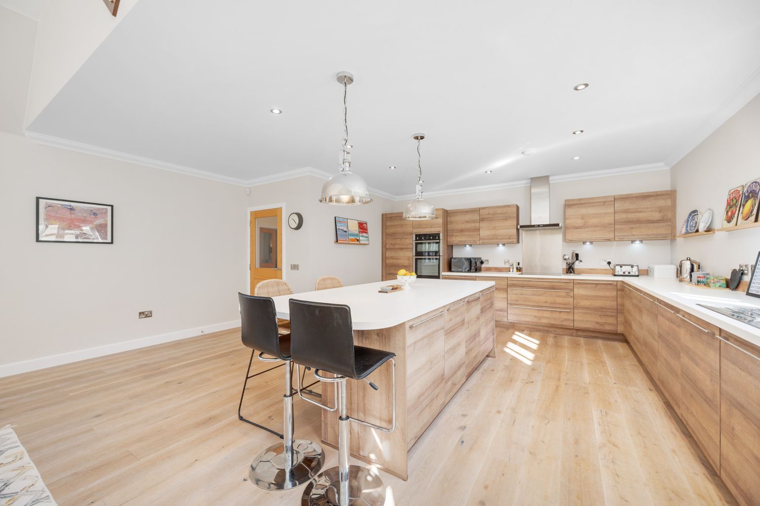 Modern kitchen interior with wooden cabinets, white countertops, hardwood flooring and black bar stools at the island.