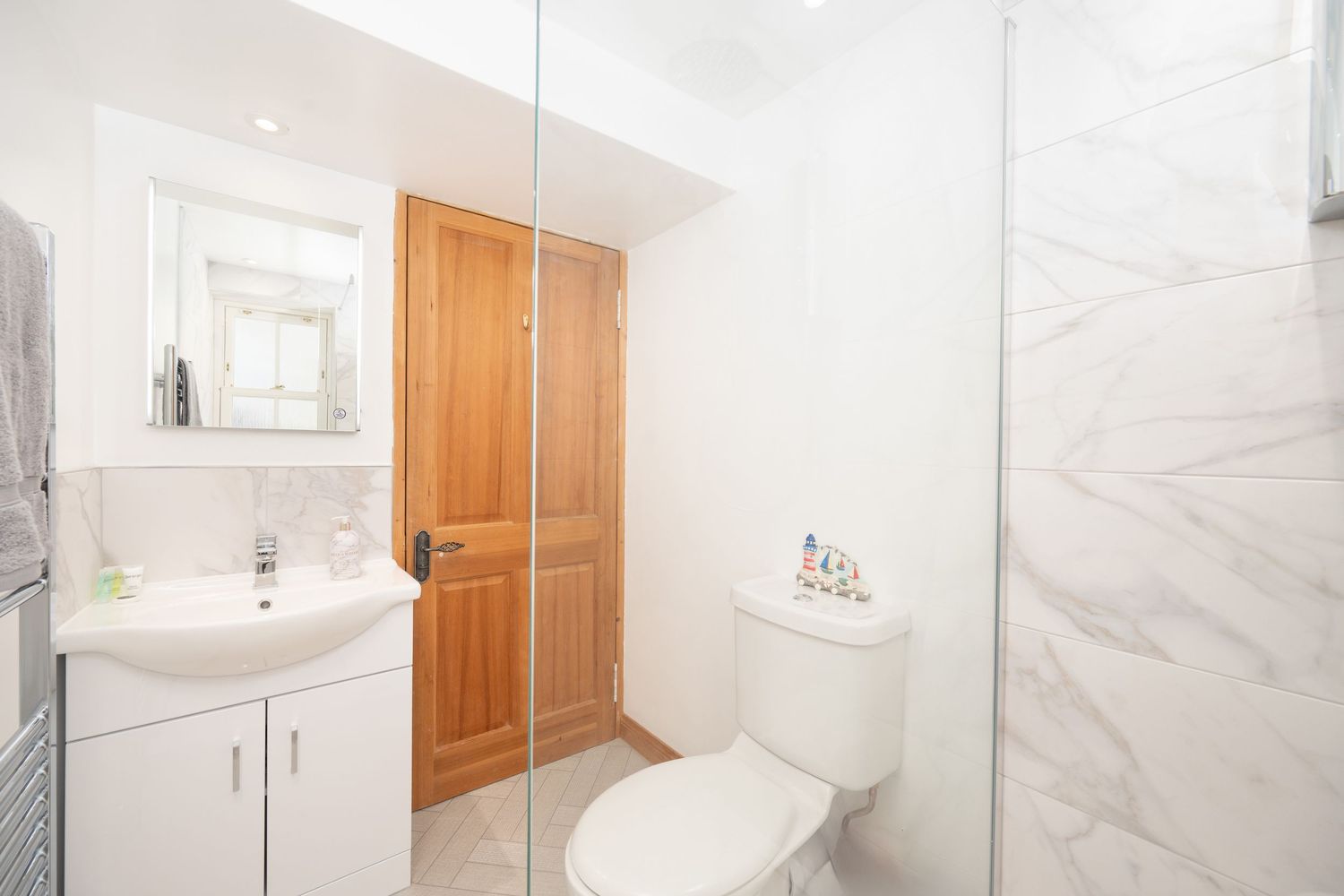 Modern bathroom interior with marble-look tiles, glass shower enclosure and wooden accents.