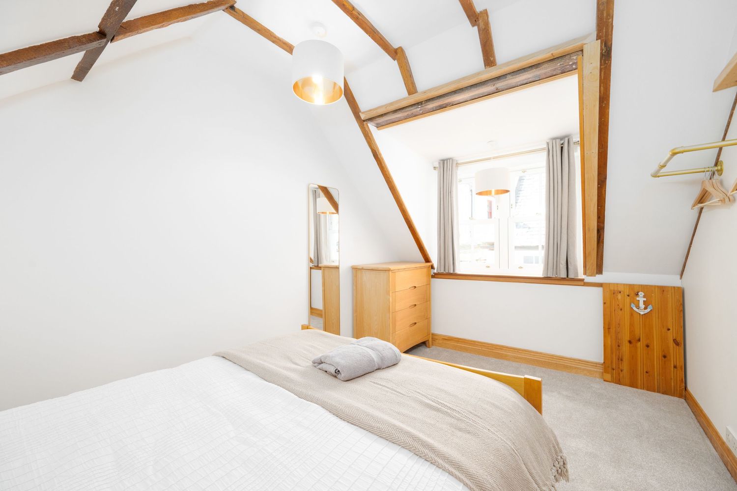 Cozy attic bedroom with exposed wooden beams, white walls, and natural light from a window.