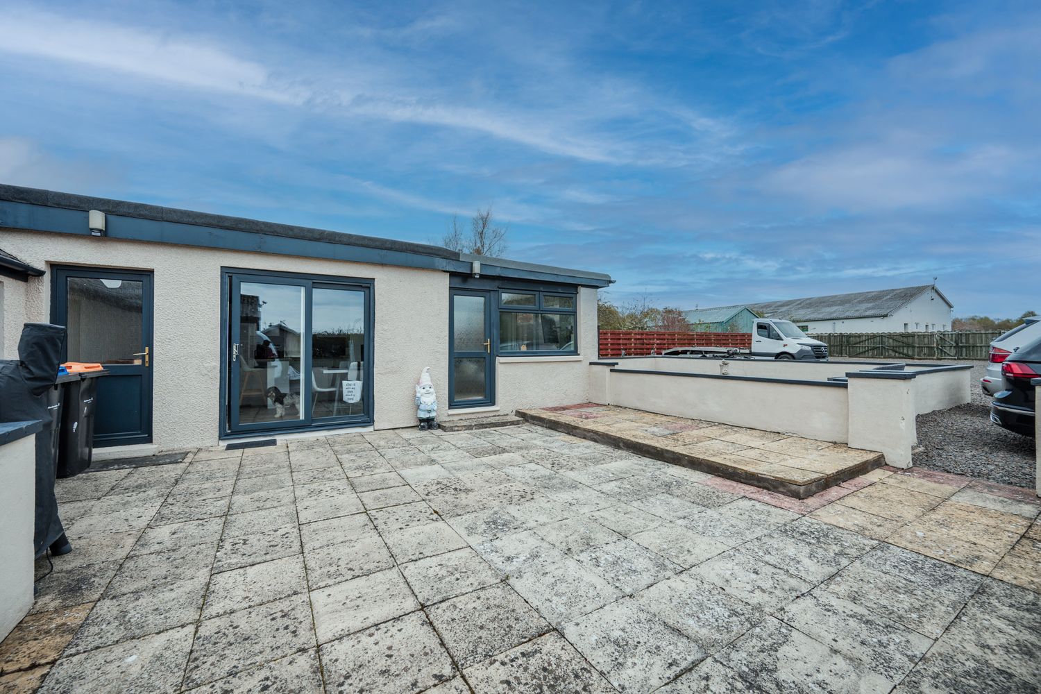 Modern rooftop terrace with textured concrete flooring, glass doors, and white exterior walls under blue skies.