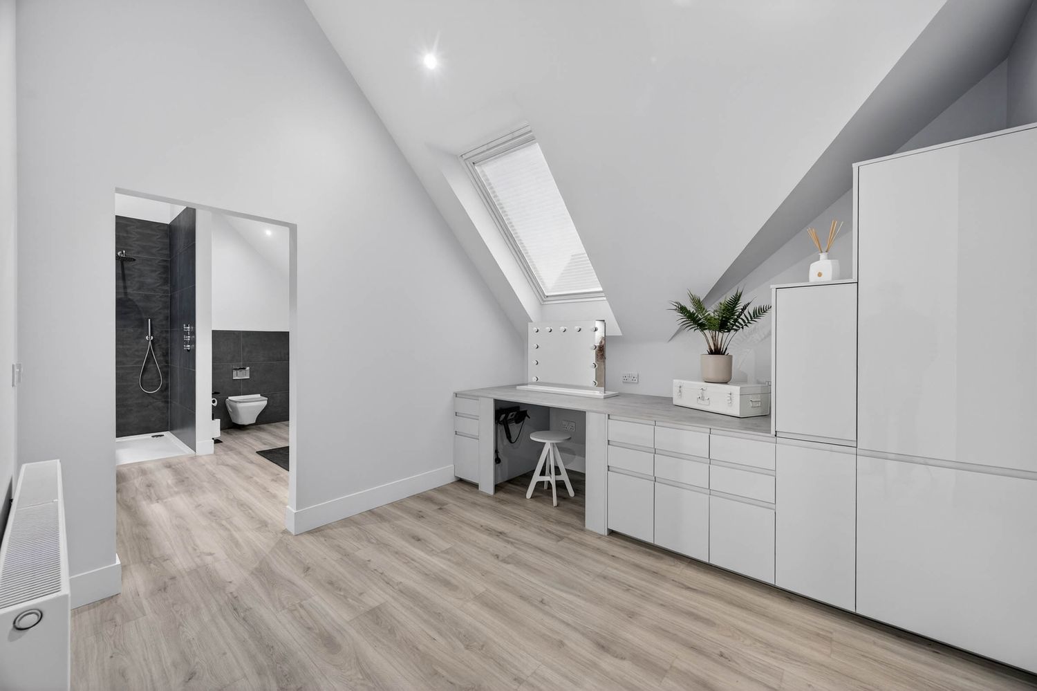 Modern attic bedroom with white walls, light wood flooring, built-in storage, and a skylight window.