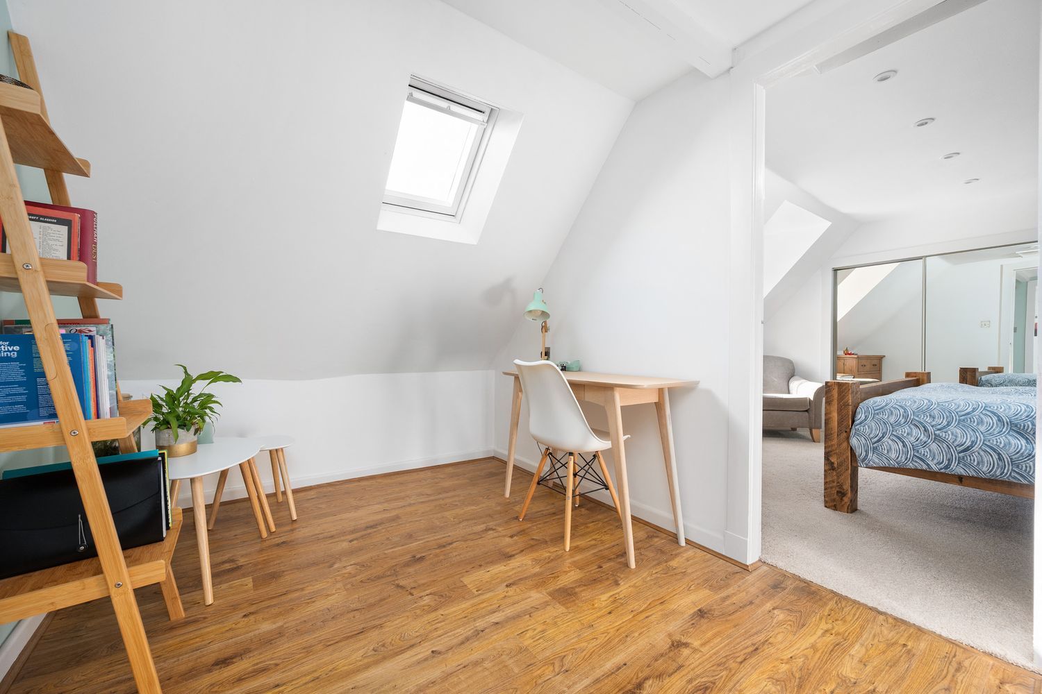 Modern attic bedroom and office space with wooden floors, skylights, and minimalist furniture in white interior design.