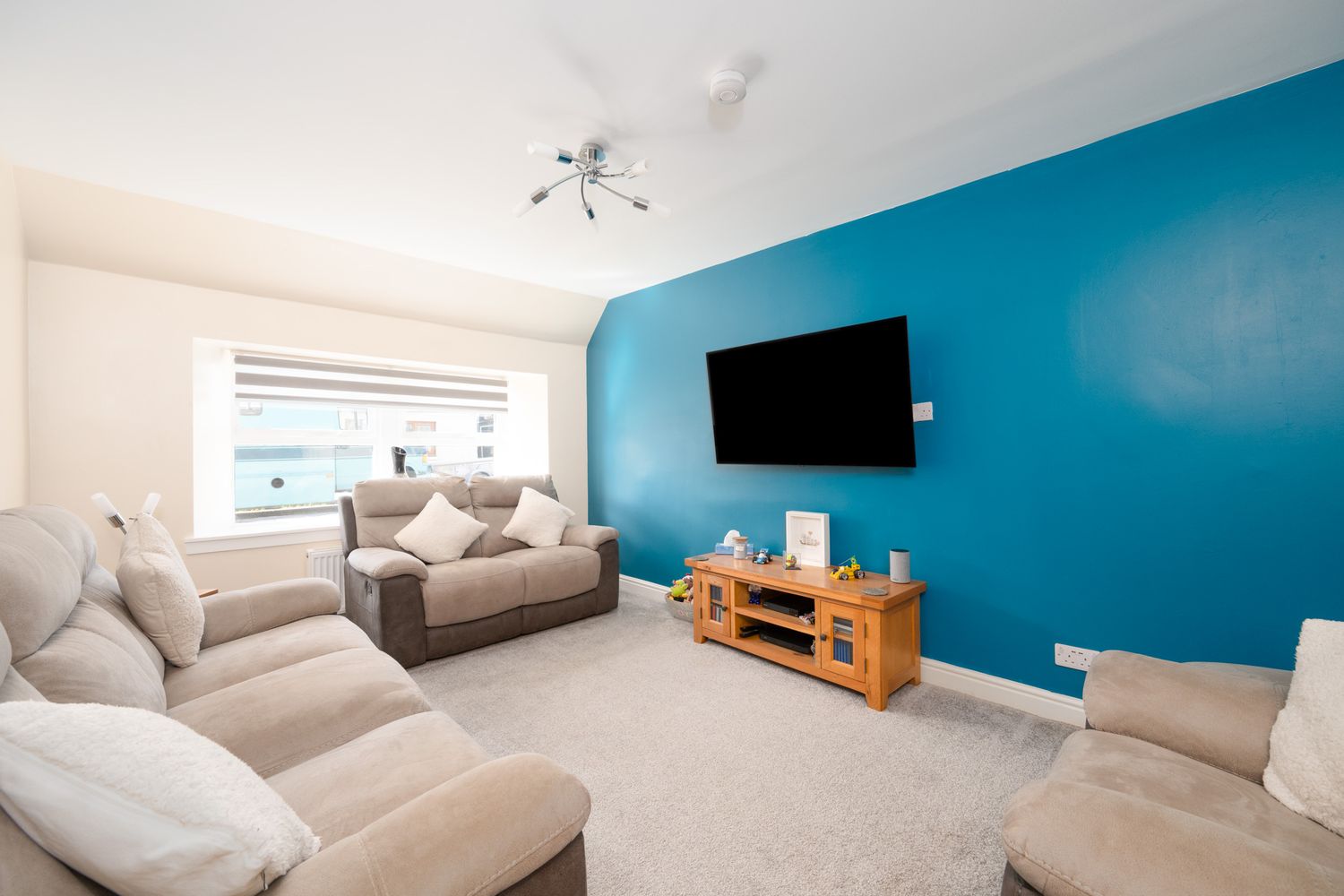 Modern living room featuring beige sofas, a wall-mounted TV, and striking turquoise accent wall with contemporary lighting.