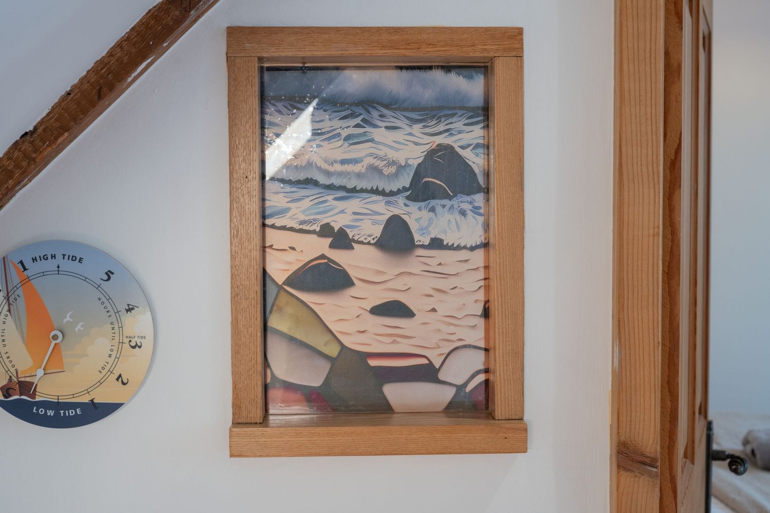Framed coastal artwork depicting rocky beach and mountains in wooden frame on white wall.