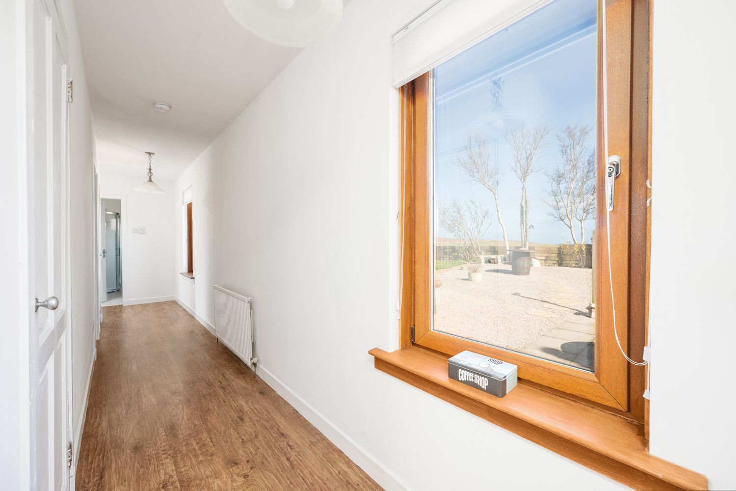 Modern hallway interior with wood flooring and large window featuring natural light and white walls.