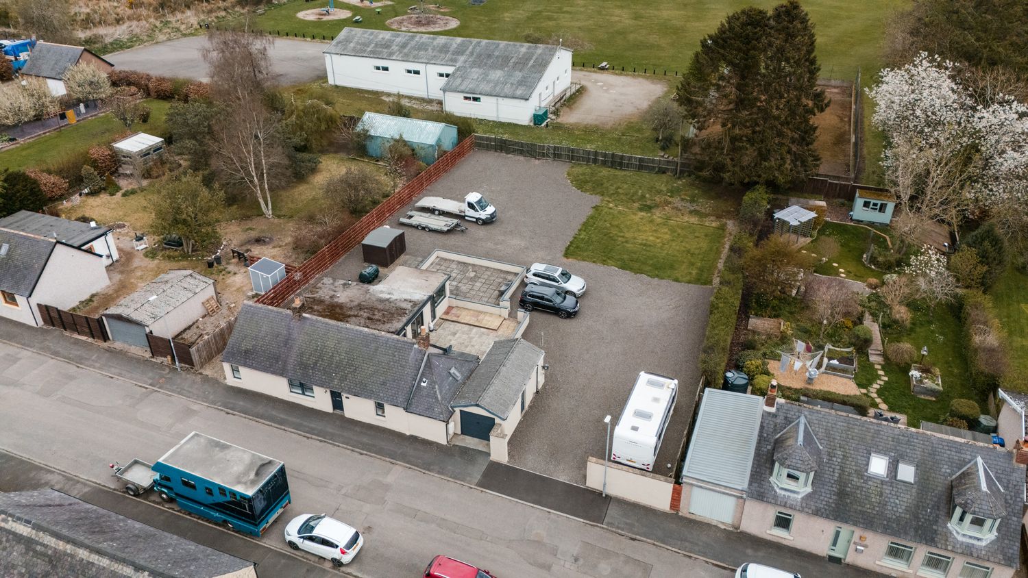 Aerial drone view of a small parking lot with vehicles and commercial buildings in a suburban setting.