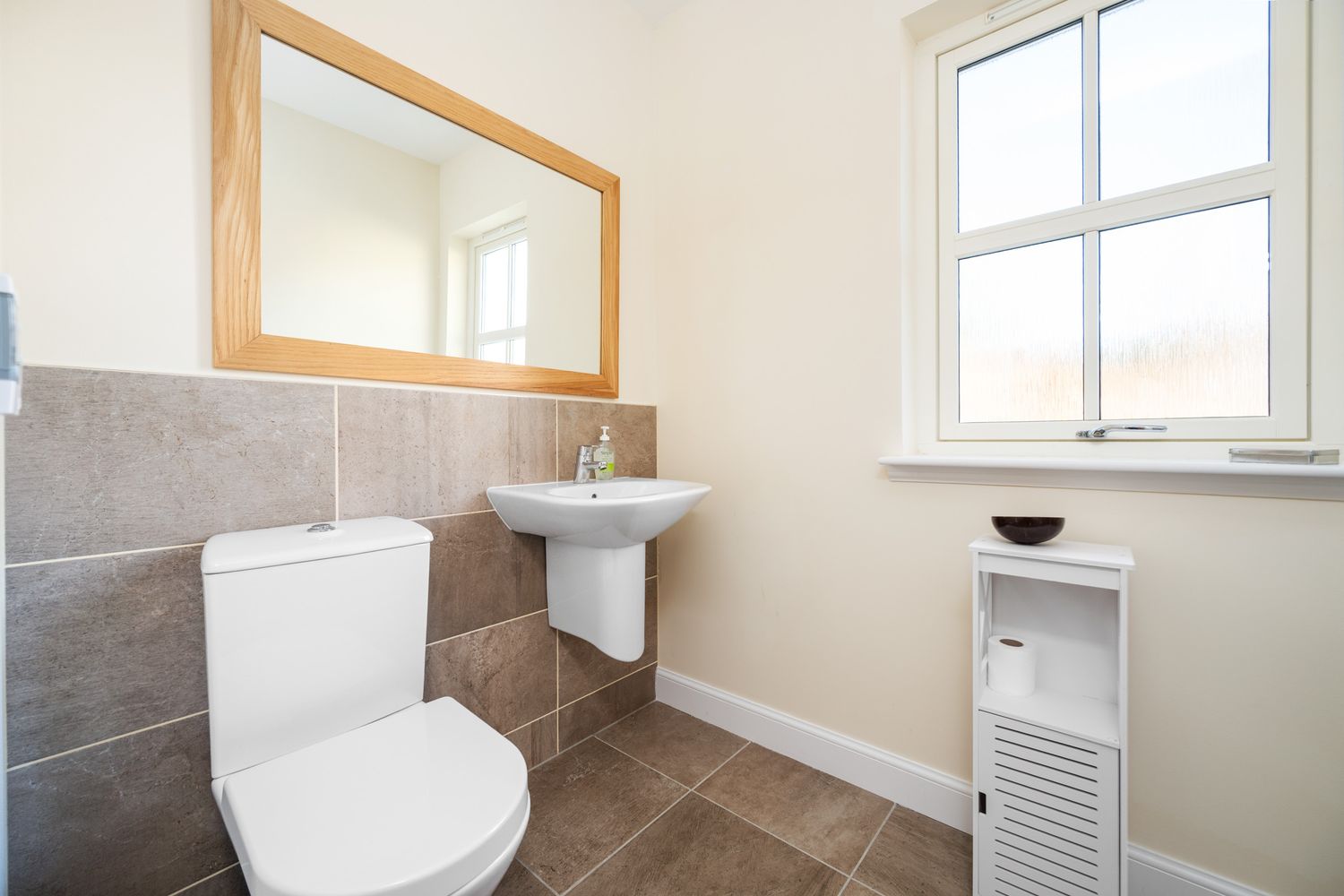 Contemporary bathroom featuring gray tile, white fixtures, and a wooden-framed mirror above the sink.