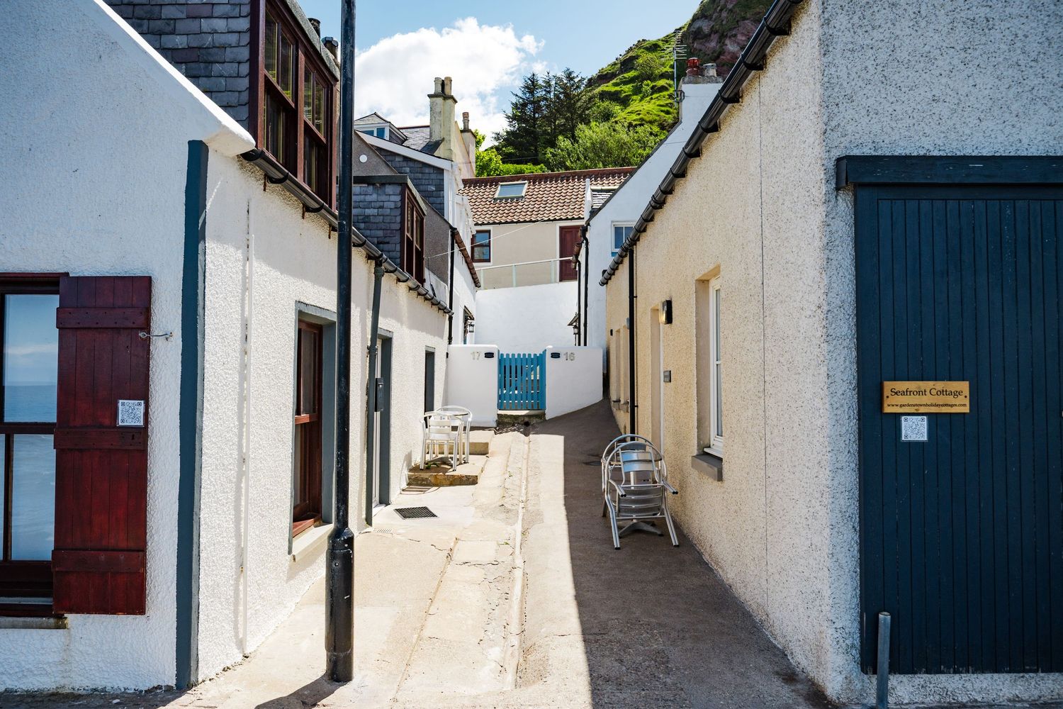 Row of whitewashed buildings along a steep coastal alley with black doors and shutters.