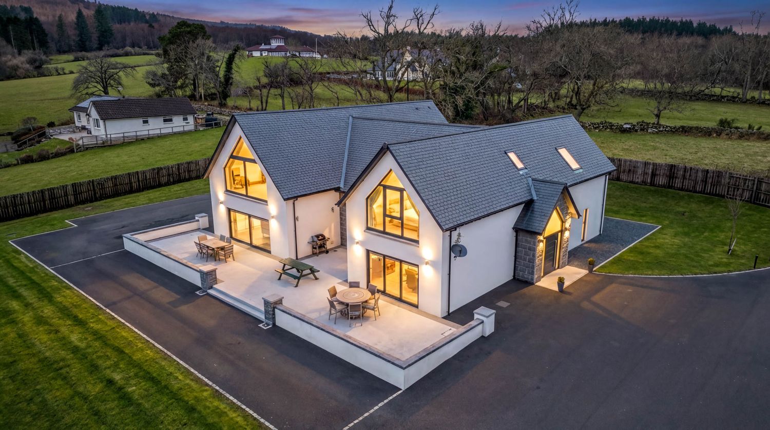 Aerial twilight view of a modern white house with illuminated windows in a rural setting.