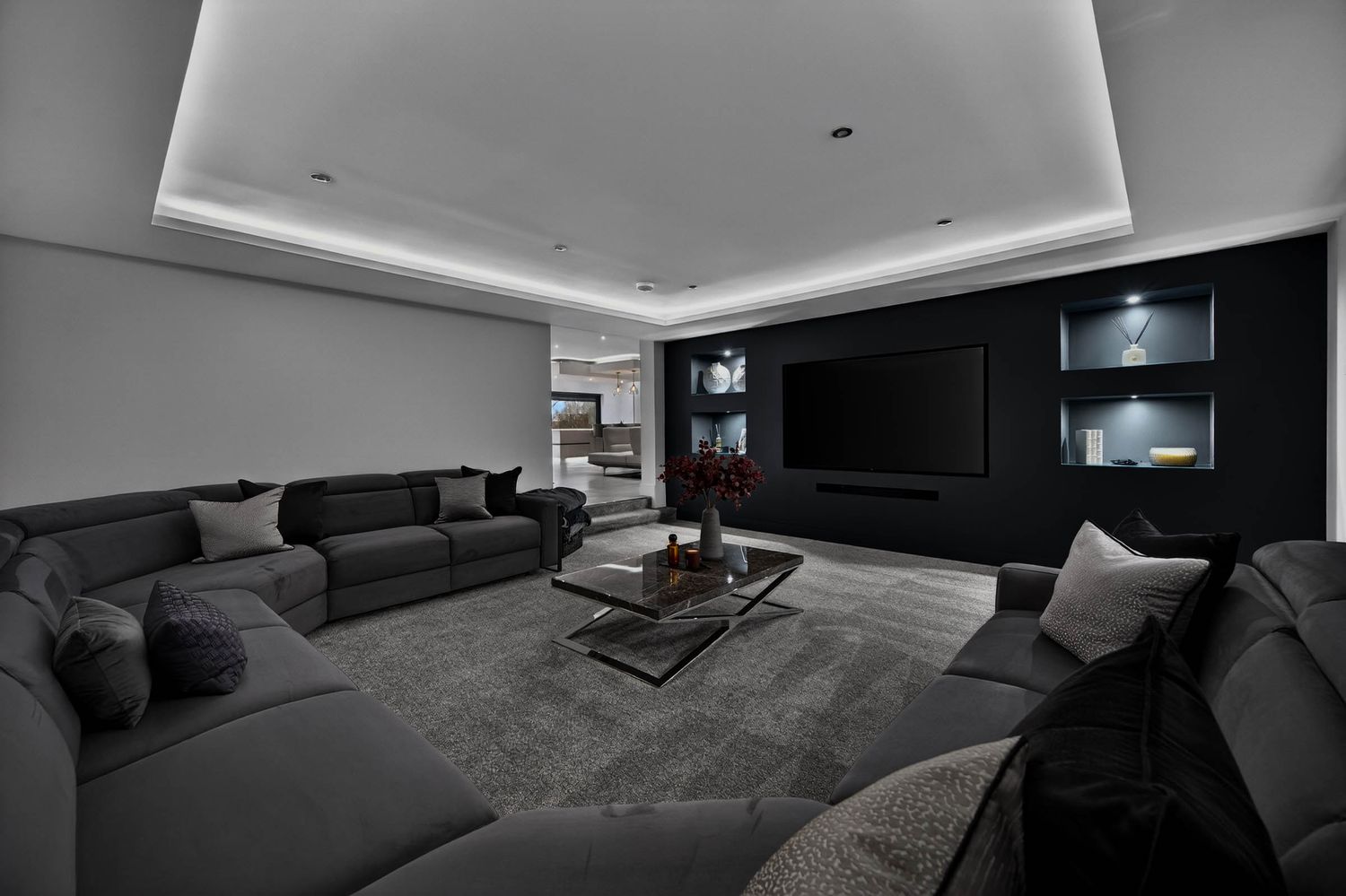 Modern home theater room with dark sectional sofa, recessed lighting, and black entertainment wall in moody lighting.