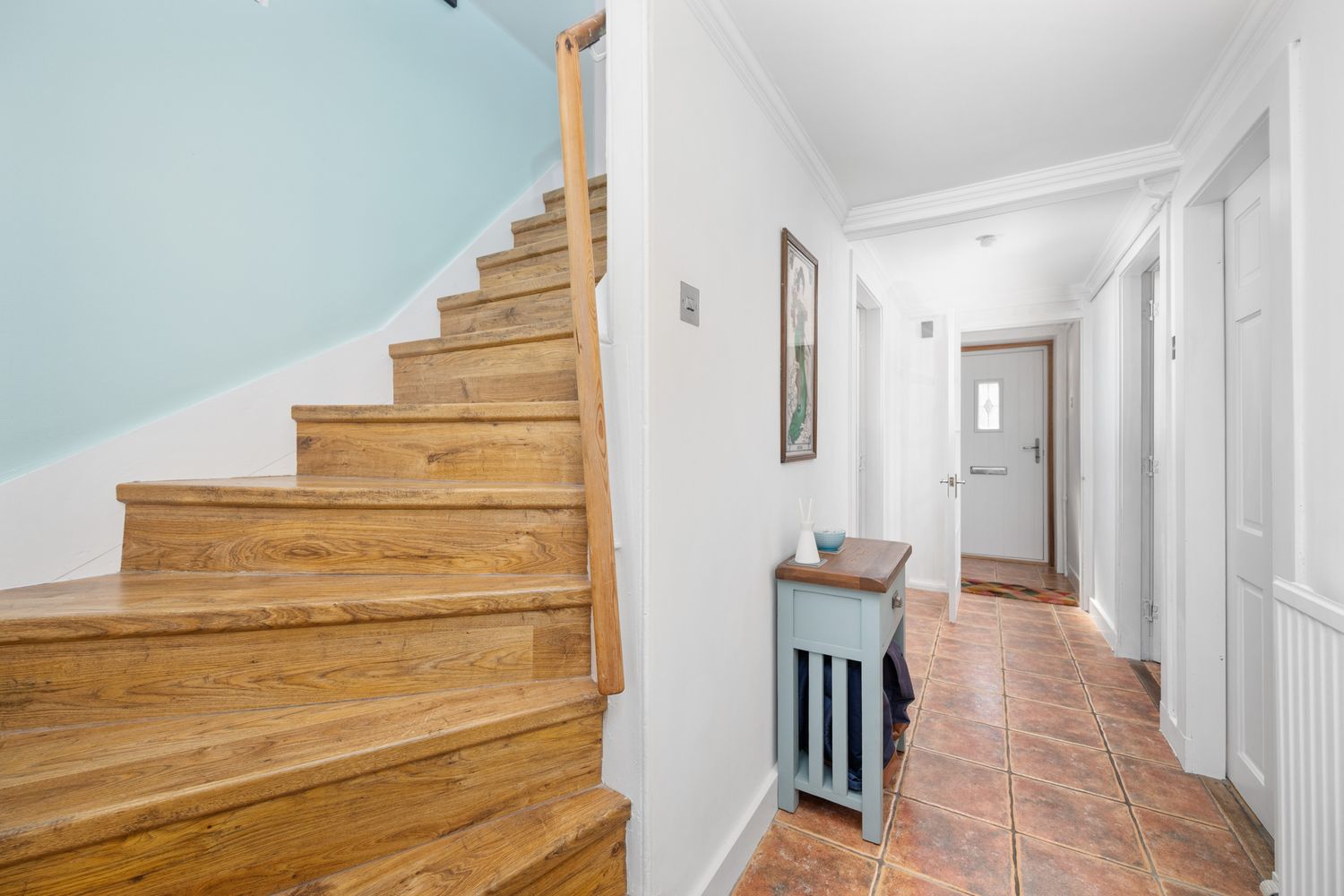 Interior hallway with terra cotta tile flooring and wooden staircase featuring natural wood steps against light blue walls.