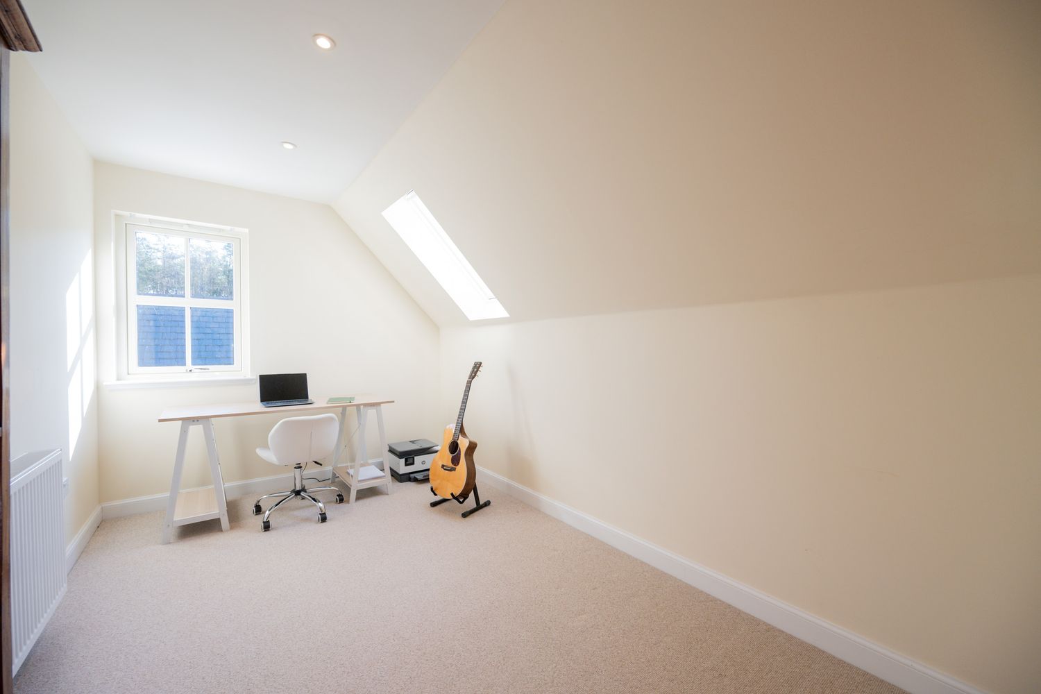 Clean white attic home office with skylights, desk setup and acoustic guitar against the wall.
