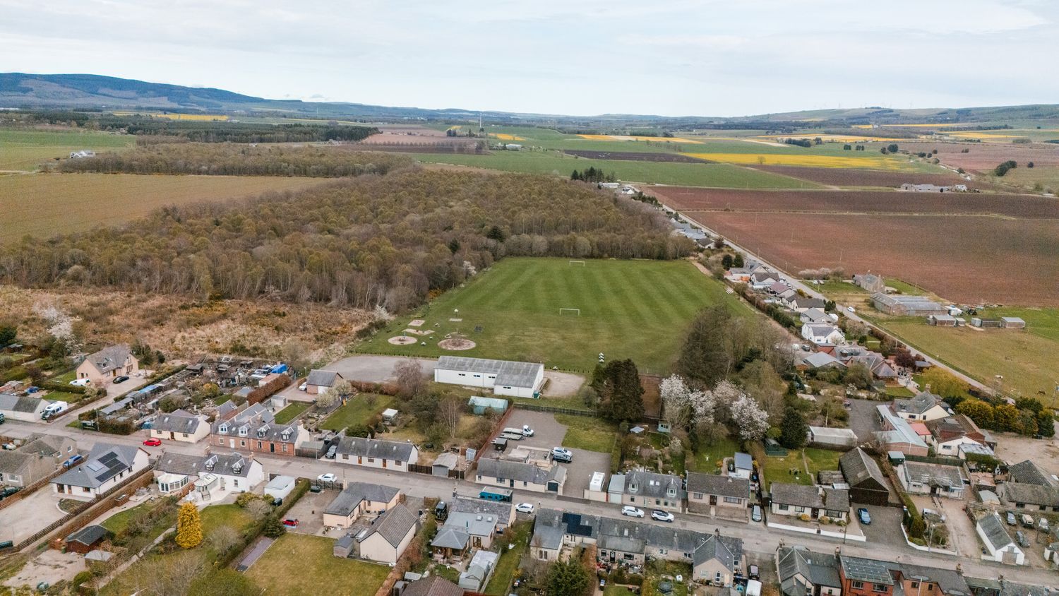 Aerial view of a small rural town with sports fields and surrounding farmland in the Scottish countryside.