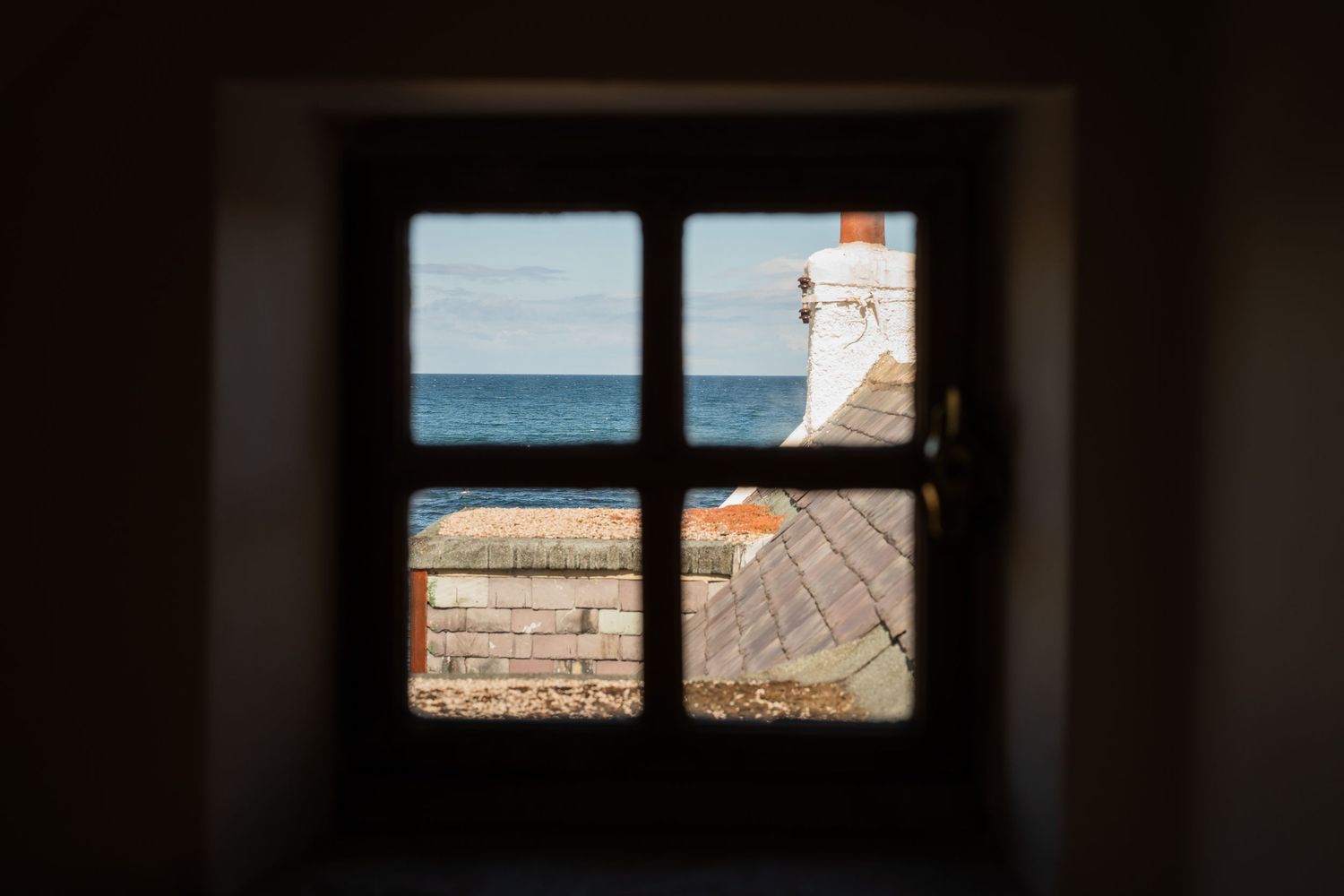 Ocean view through a dark window frame showing coastal scenery and clear blue water.