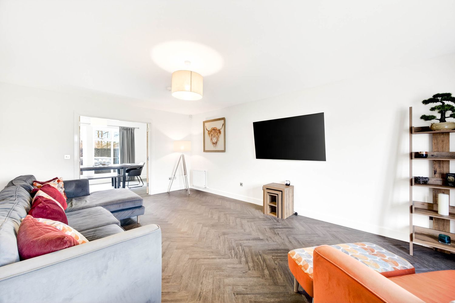 Modern living room with herringbone flooring, grey sectional sofa, and wall-mounted TV.