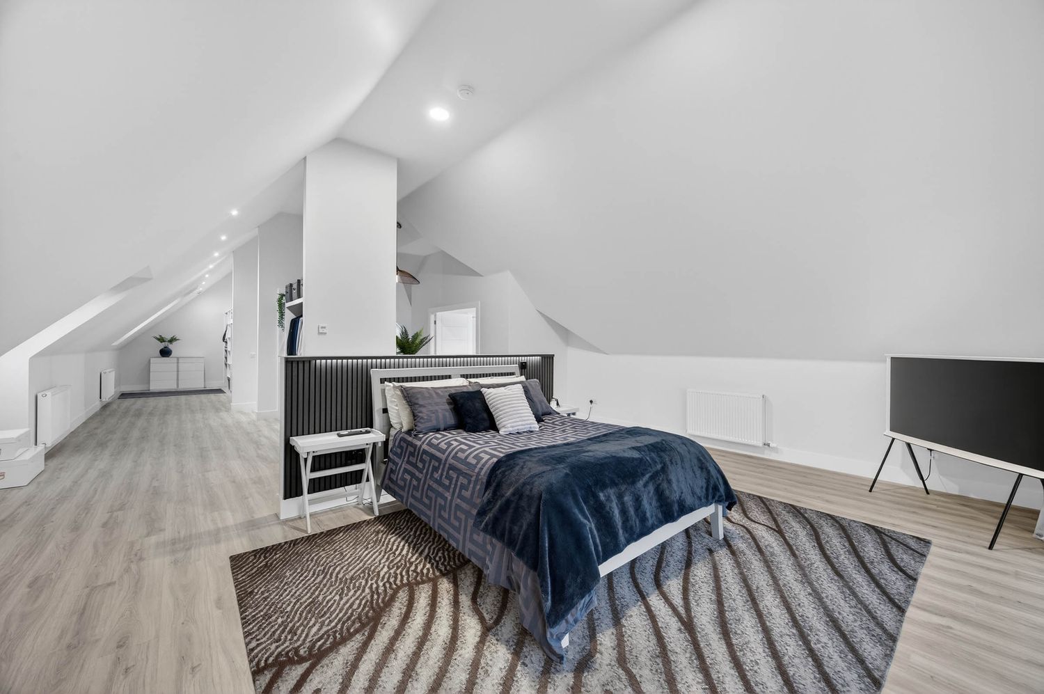 Spacious attic bedroom with gray carpet, sloped ceiling, and navy blue bedding accents.