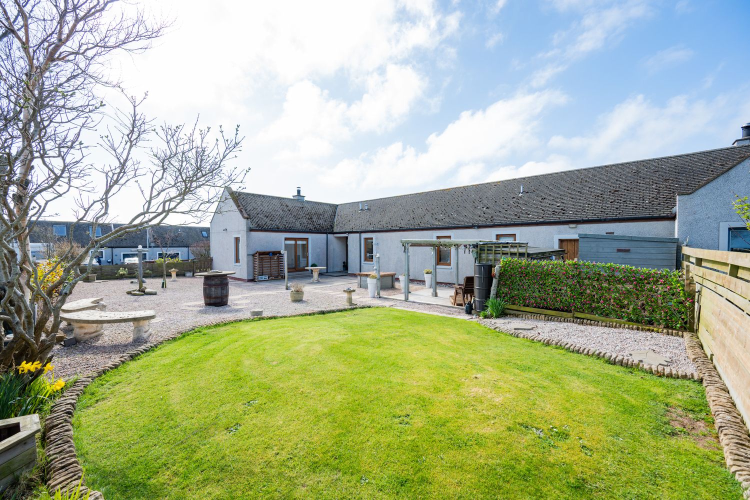 White cottage-style home with well-maintained lawn and paved patio area on sunny day with blue skies.