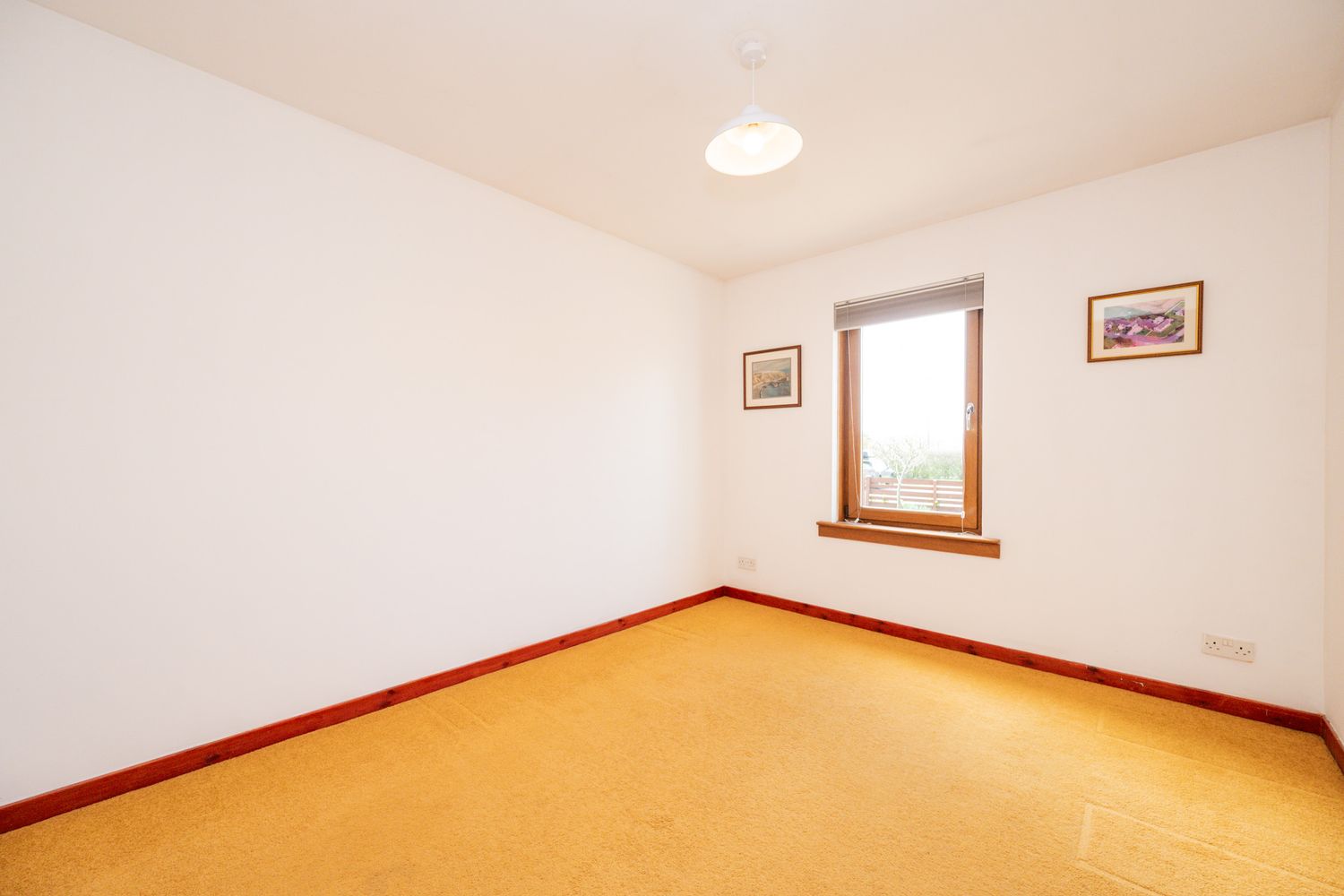 Empty bedroom with orange carpet flooring, white walls, and a small window with wooden frame.