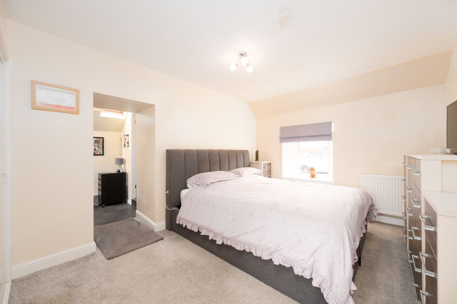 Spacious contemporary bedroom with gray upholstered headboard, white bedding, and carpet flooring.