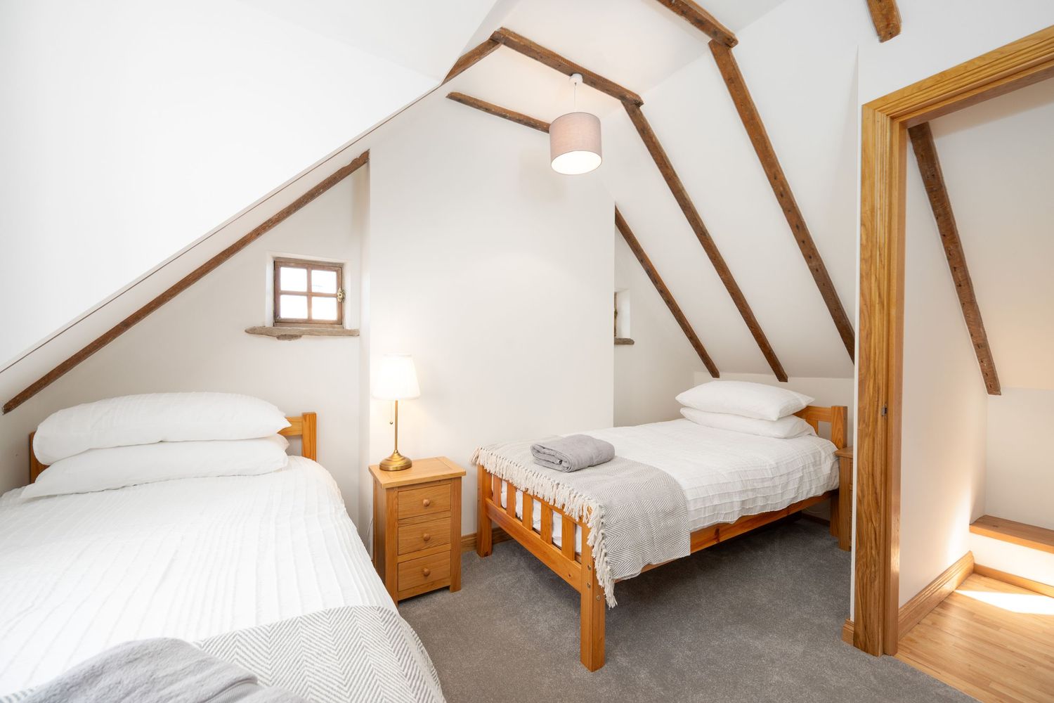 Twin bedroom in attic space with wooden beams, white walls and matching wooden bed frames.
