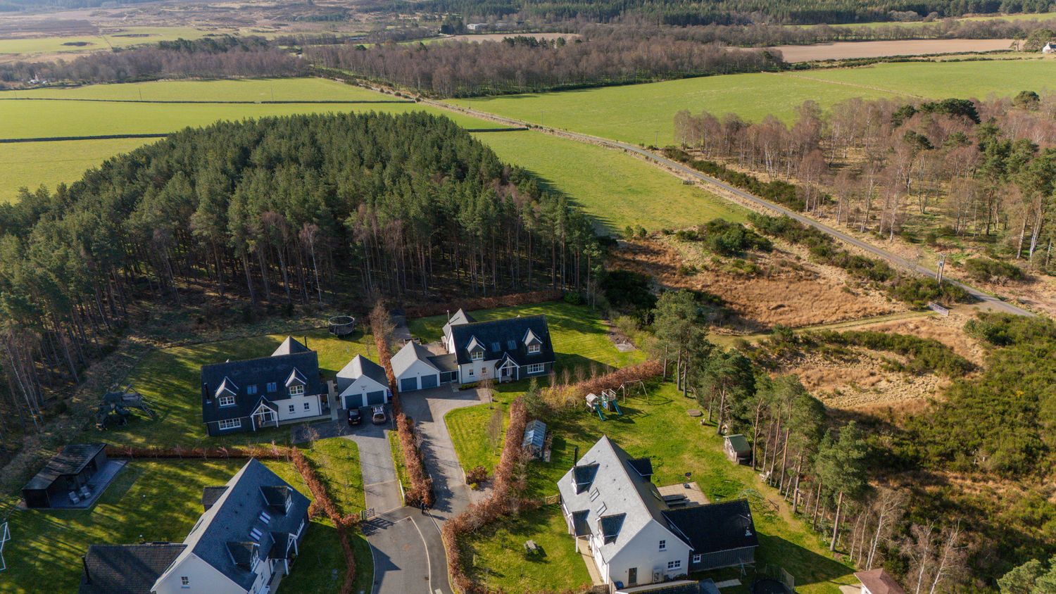 Aerial view of luxury homes nestled among pine trees with green farmland and rolling countryside in the background.