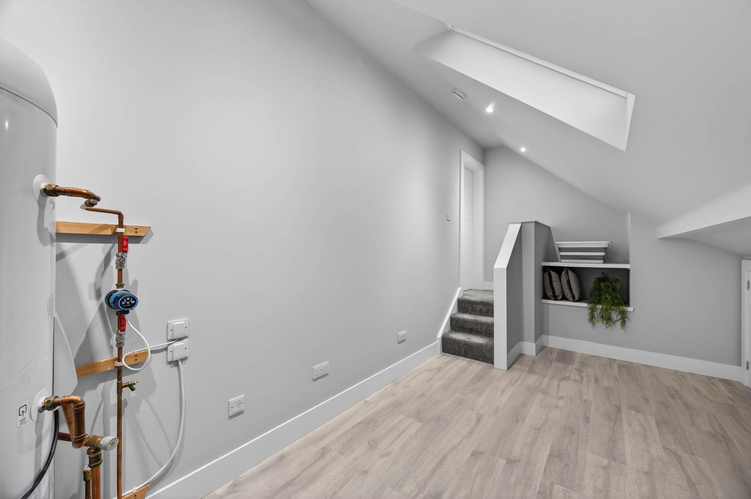 Modern attic office space with white walls, wood flooring, and skylight windows.