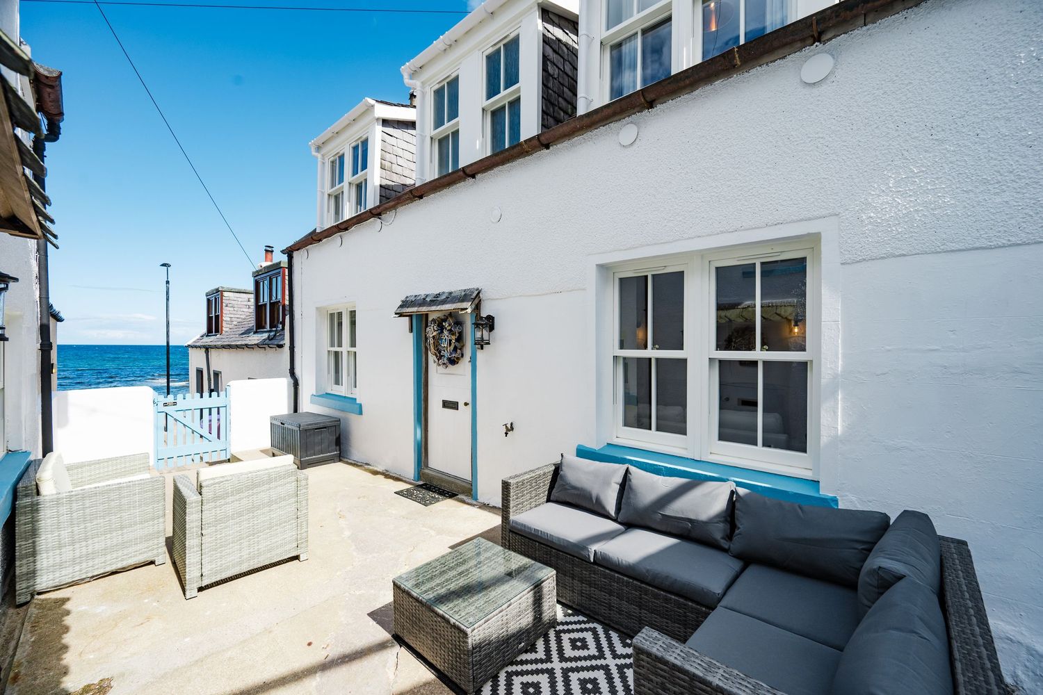 Seaside terrace with grey outdoor seating and ocean views framed by white coastal architecture.