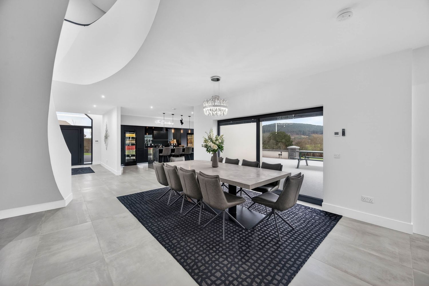 Modern minimalist living room features sleek white walls, polished floors, and a navy blue geometric area rug.