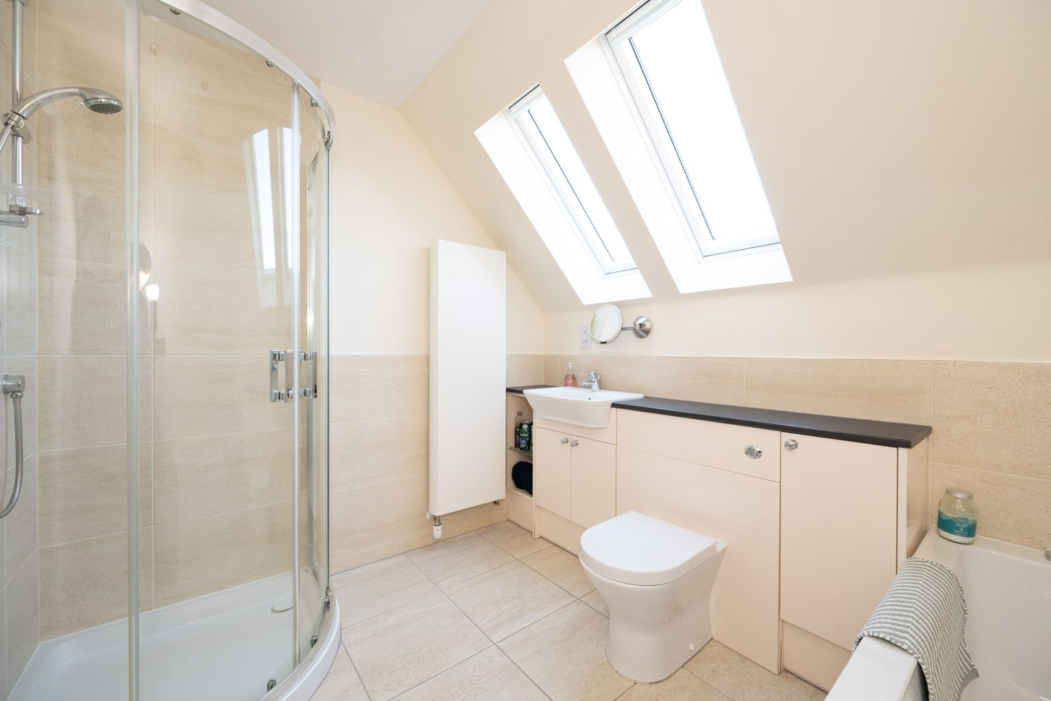 Modern attic bathroom with curved glass shower enclosure, white fixtures, and skylights providing natural illumination.