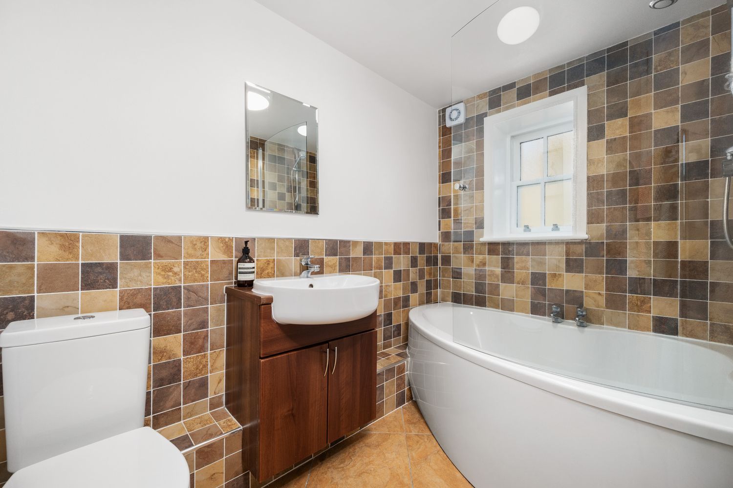 Contemporary bathroom featuring brown mosaic tiling, curved bathtub, white sink and wooden vanity unit.