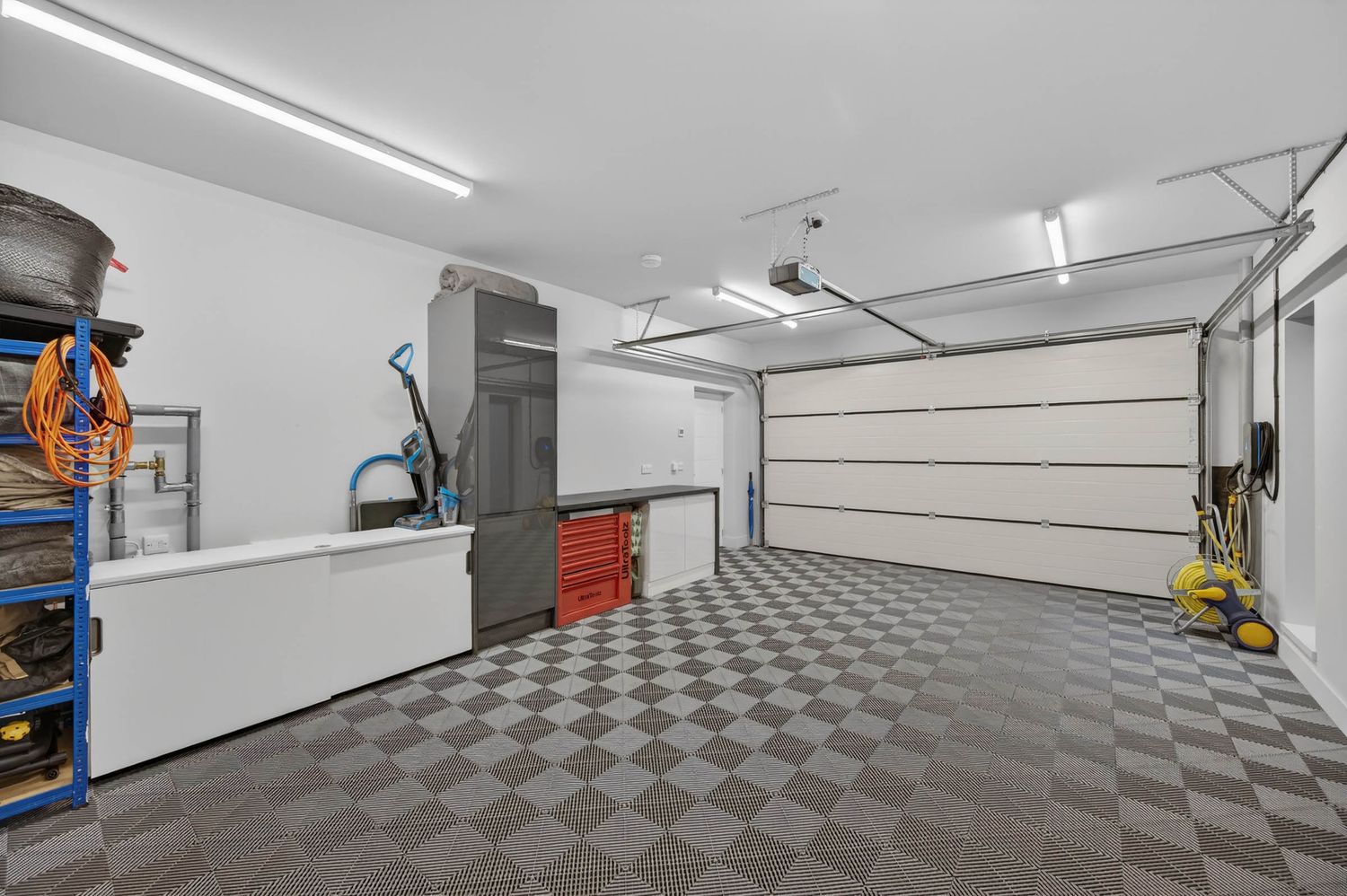 Clean modern garage interior with checkered floor tiles and bright fluorescent lighting shows organized storage space.