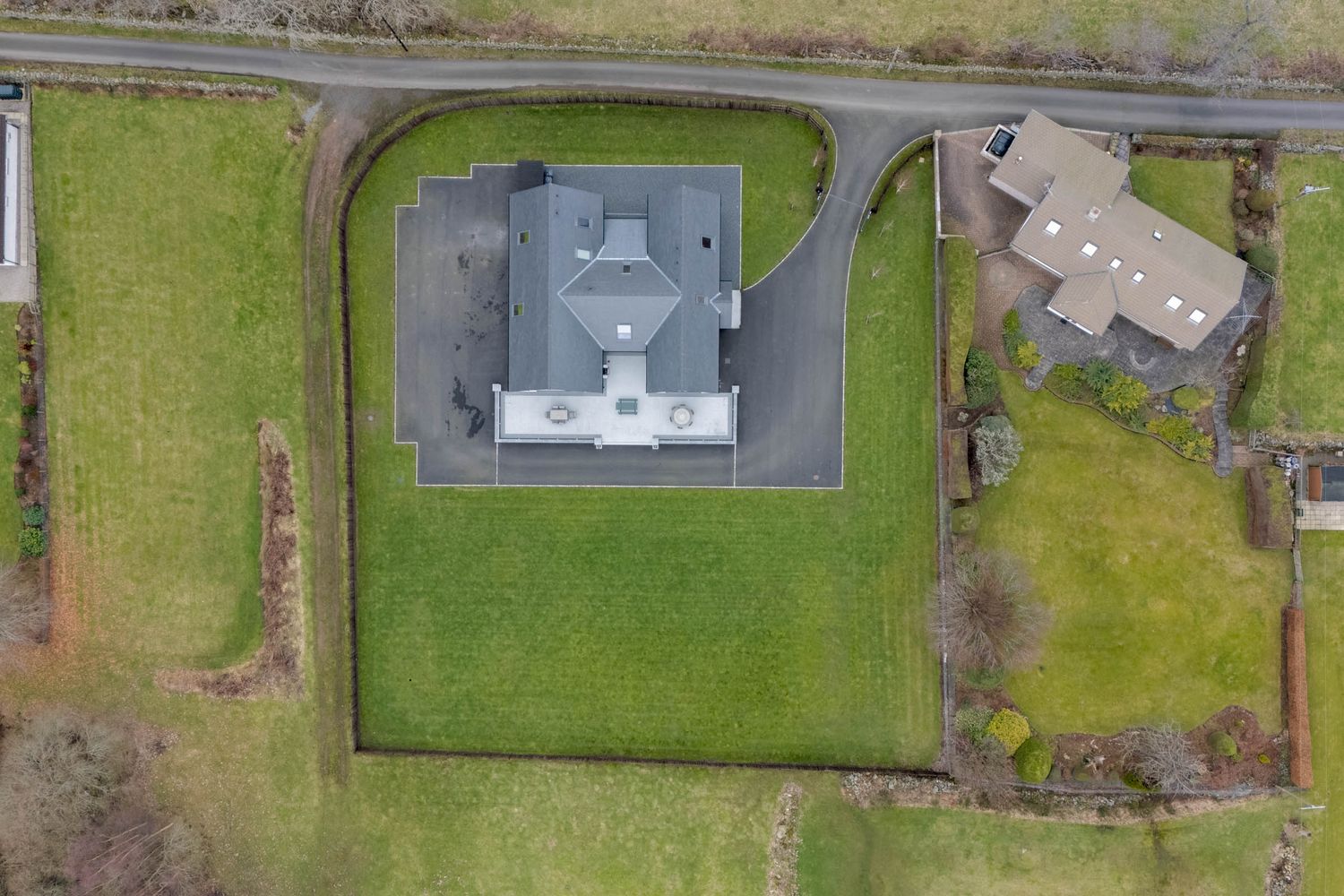 Bird's eye view of multiple properties with green lawns and driveways separated by hedgerows.