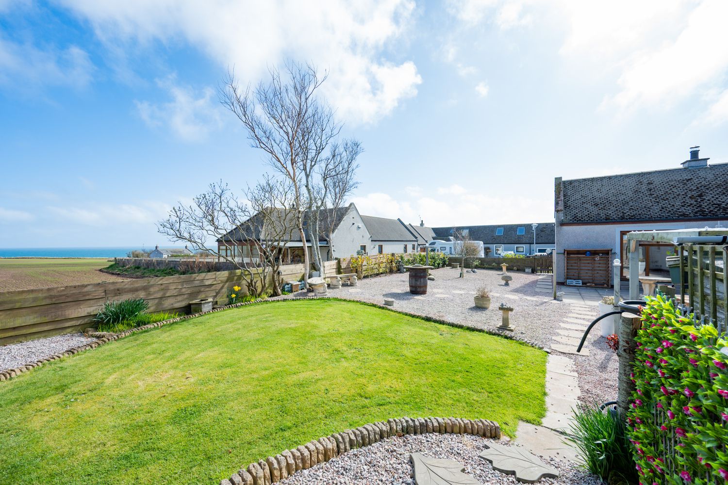 Modern waterfront property in Scotland with manicured lawn and patio area overlooking the ocean on a sunny day.