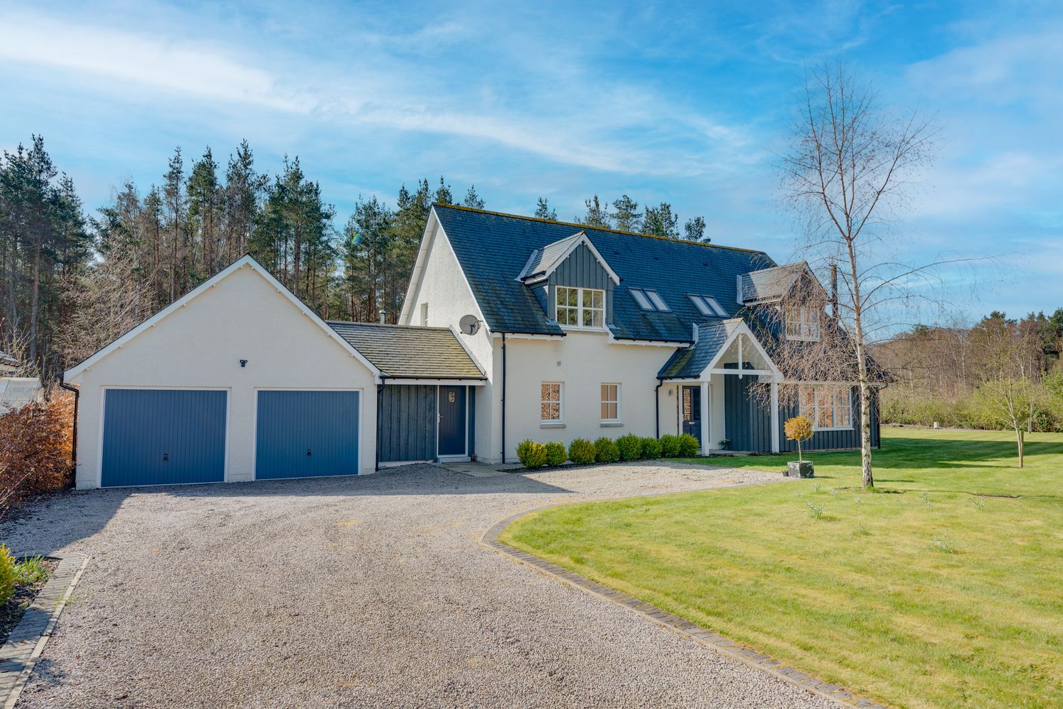 Modern white country house with blue roof and attached two-car garage situated on a landscaped garden with gravel driveway.