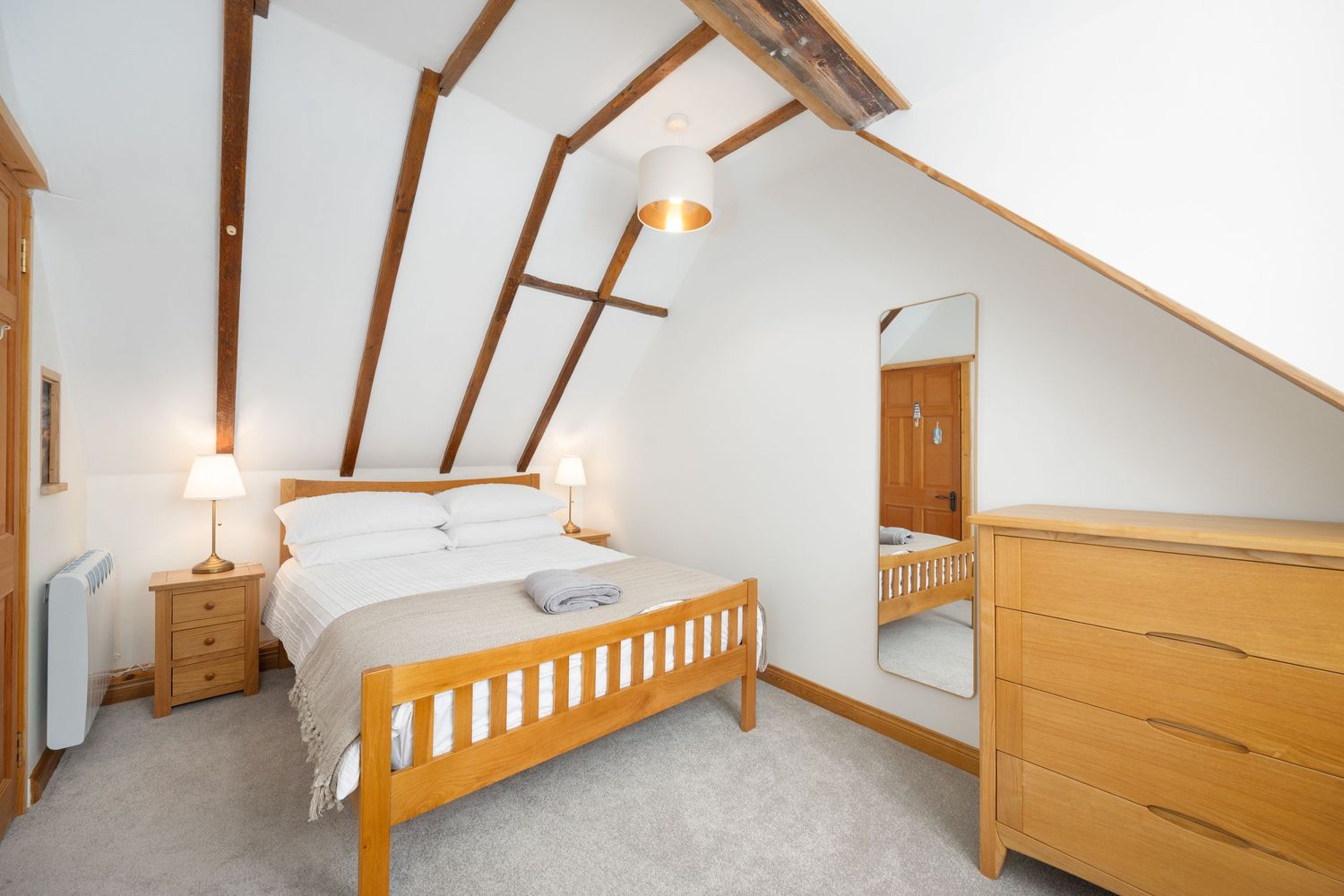 Bright modern attic bedroom with wooden beams and sloped ceiling featuring comfortable sleeping space.