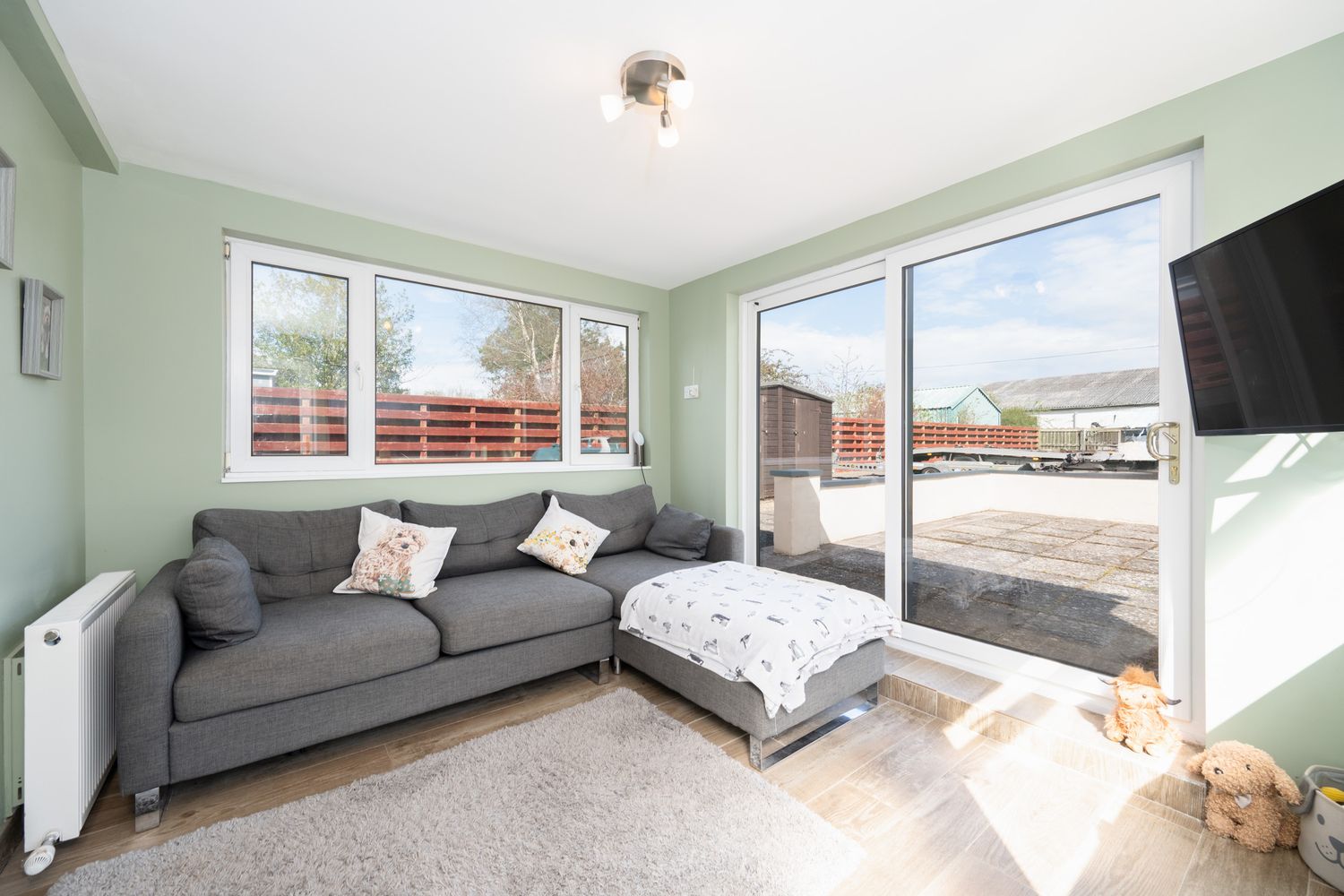 Bright modern living room with gray sofa, sliding glass doors to balcony, and wall-mounted TV against mint green walls.