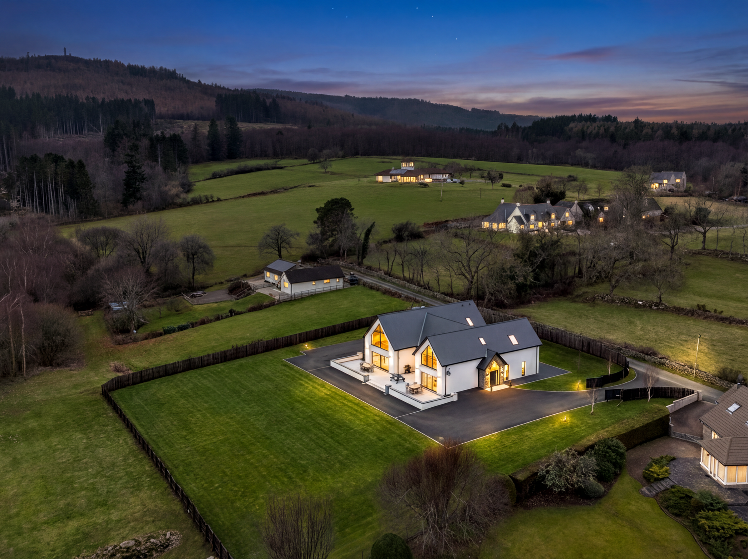 Panoramic aerial view of a countryside property with rolling hills and scattered houses at sunset.