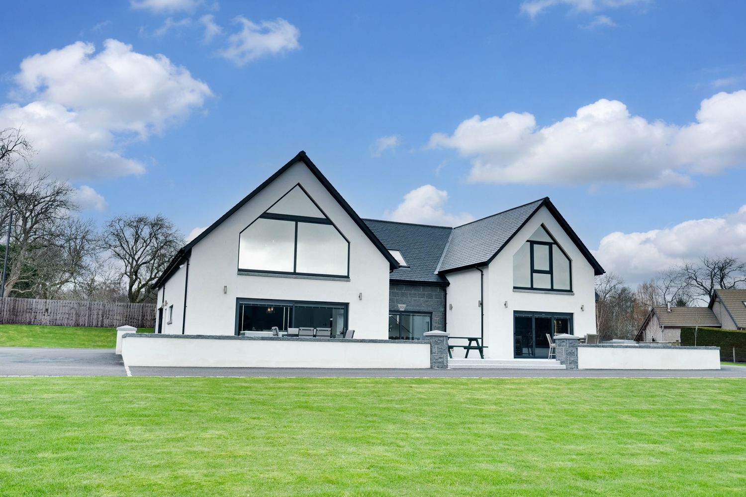 Modern white and gray farmhouse style home with large windows and manicured green lawn under blue cloudy sky.