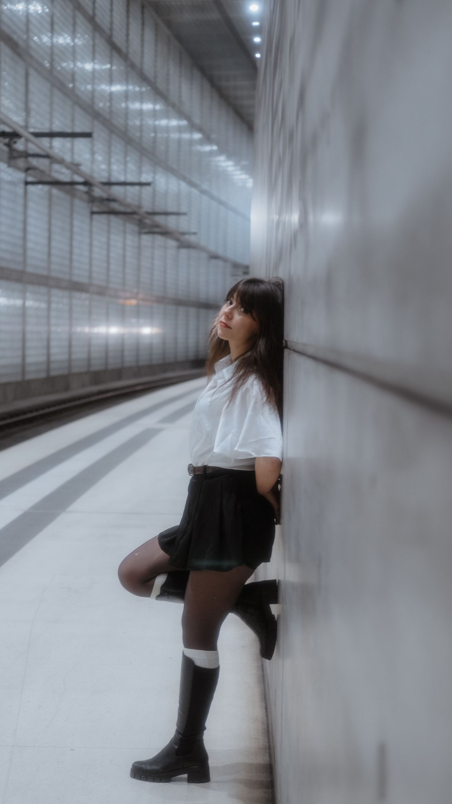 Frau wartet auf die Bahn und lehnt an weißer Wand
