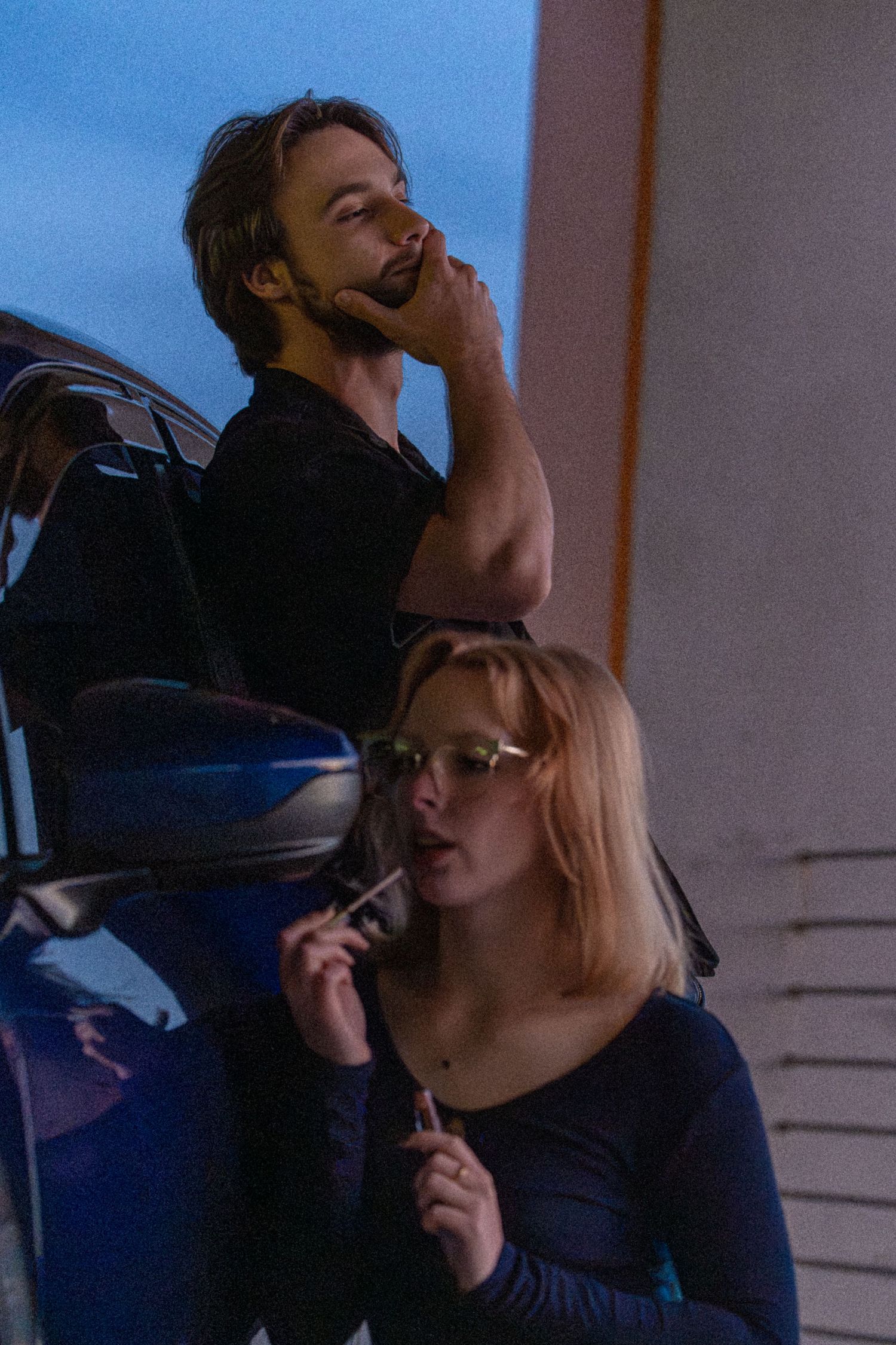 Man and woman leaning against blue car at dusk in moody evening light photography.