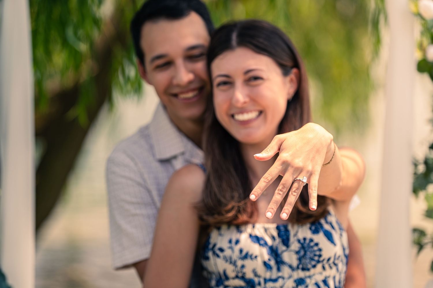 Happy couple smiling and showing off engagement ring outdoors, woman displaying diamond ring on her hand.