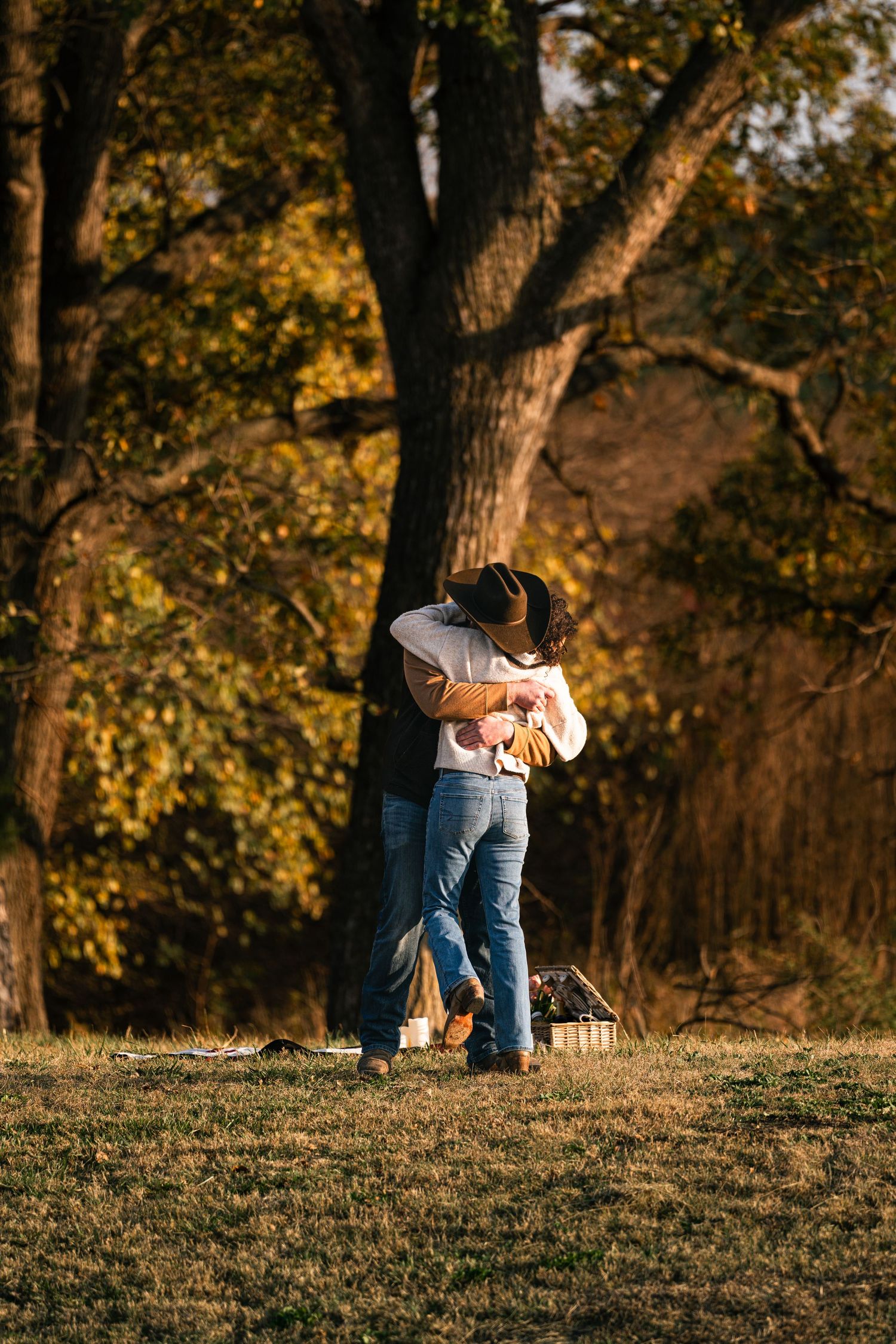 Couple embracing and kissing in a golden autumn park with tall trees and warm sunlight.