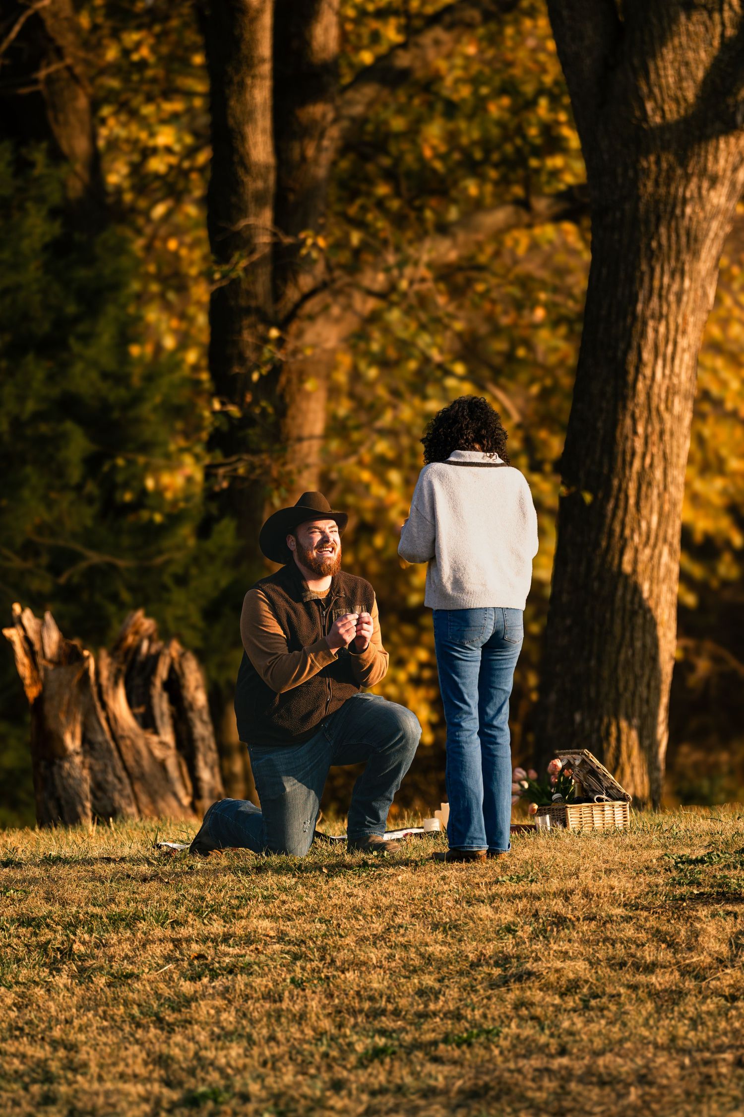 Man on one knee proposing to woman in autumn park with golden foliage at sunset.