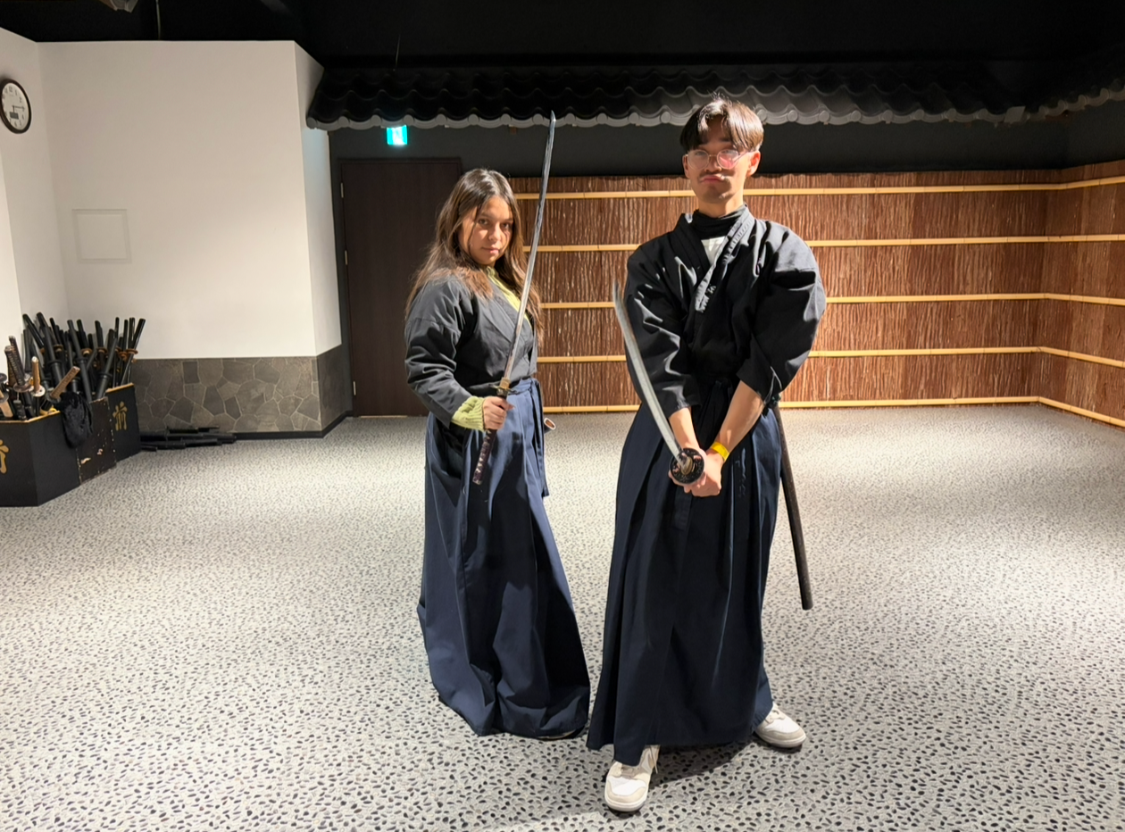 Two visitors dressed in traditional kendo uniforms holding swords at a Japanese dojo experience.