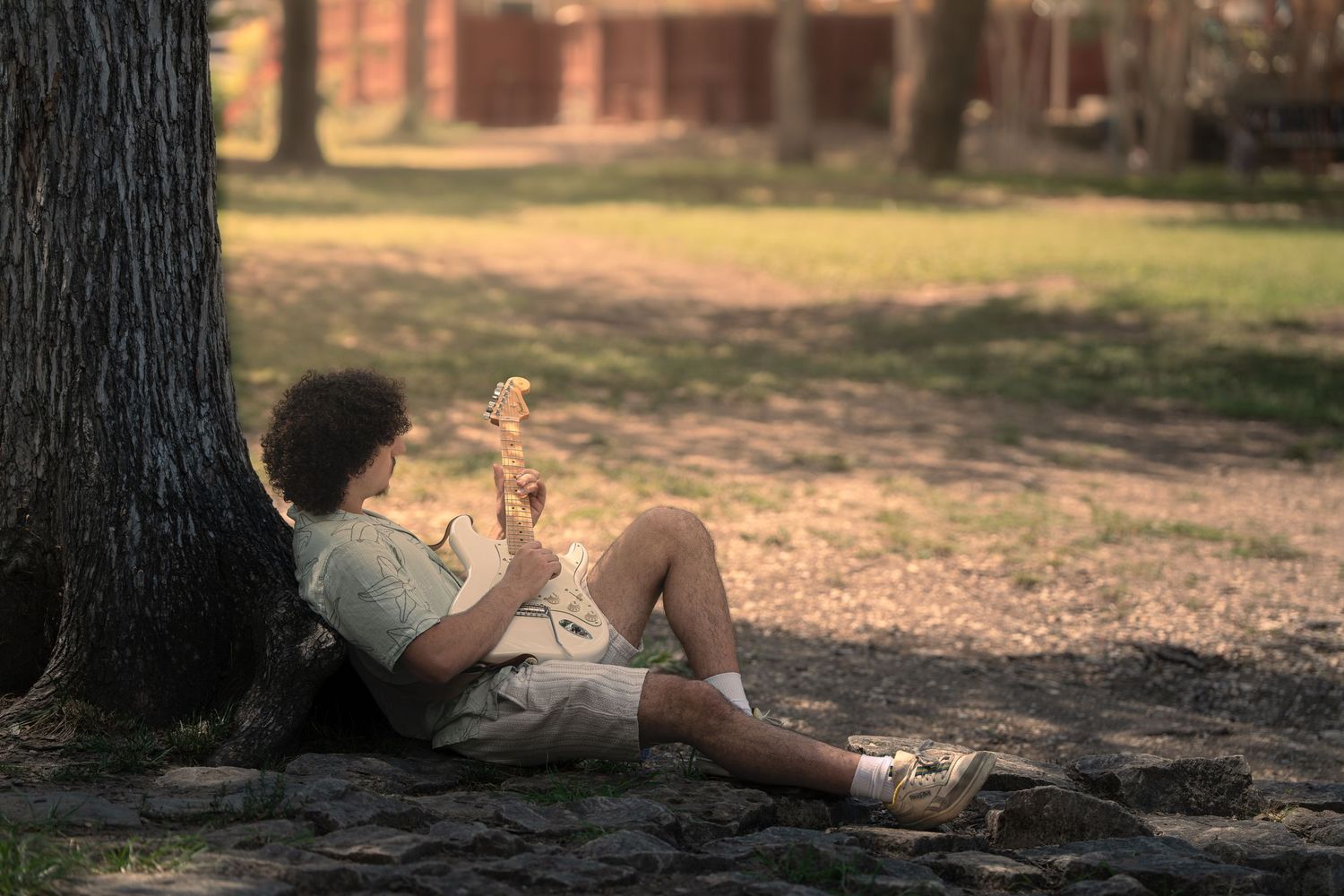 Child sitting against a tree in a park, reading a book outdoors on a sunny day.