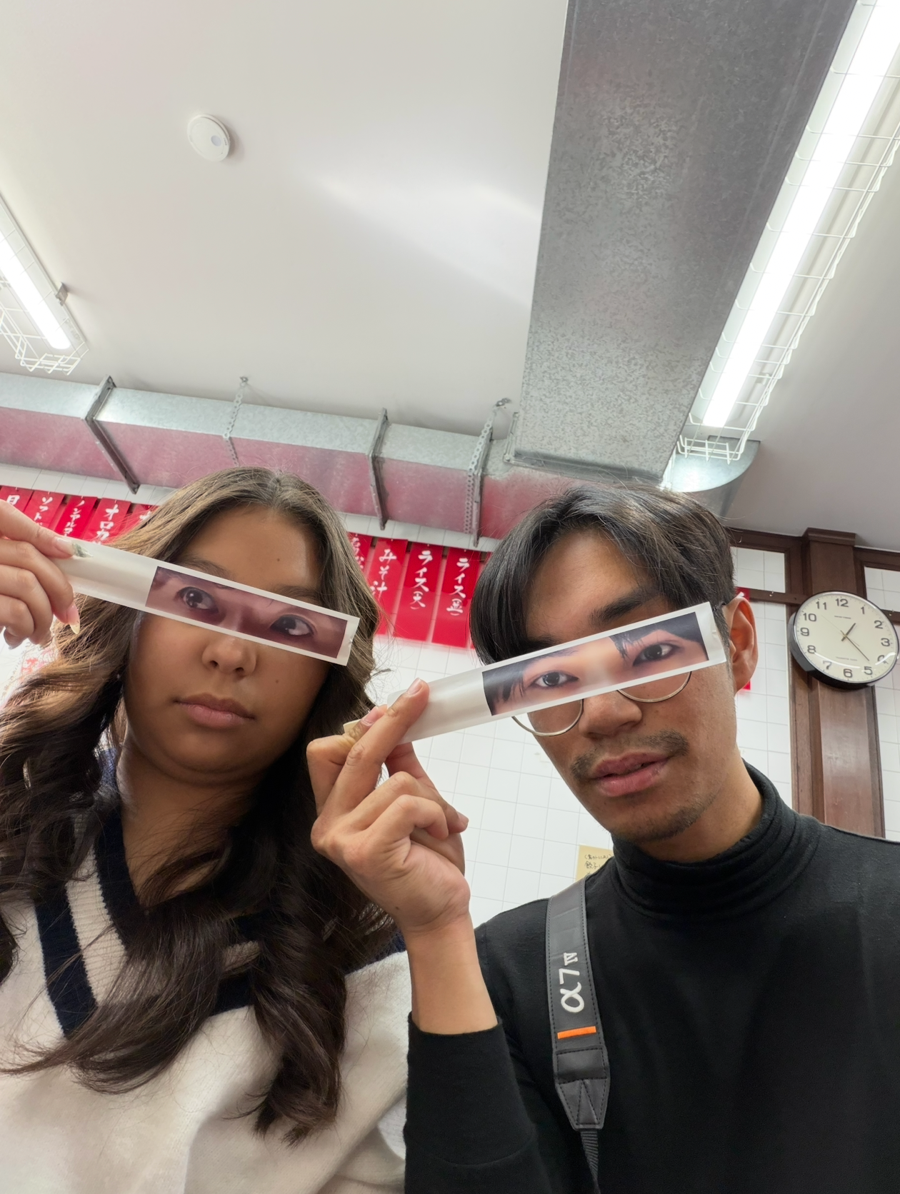 Two young people holding photo strips over their eyes as quirky glasses indoors.
